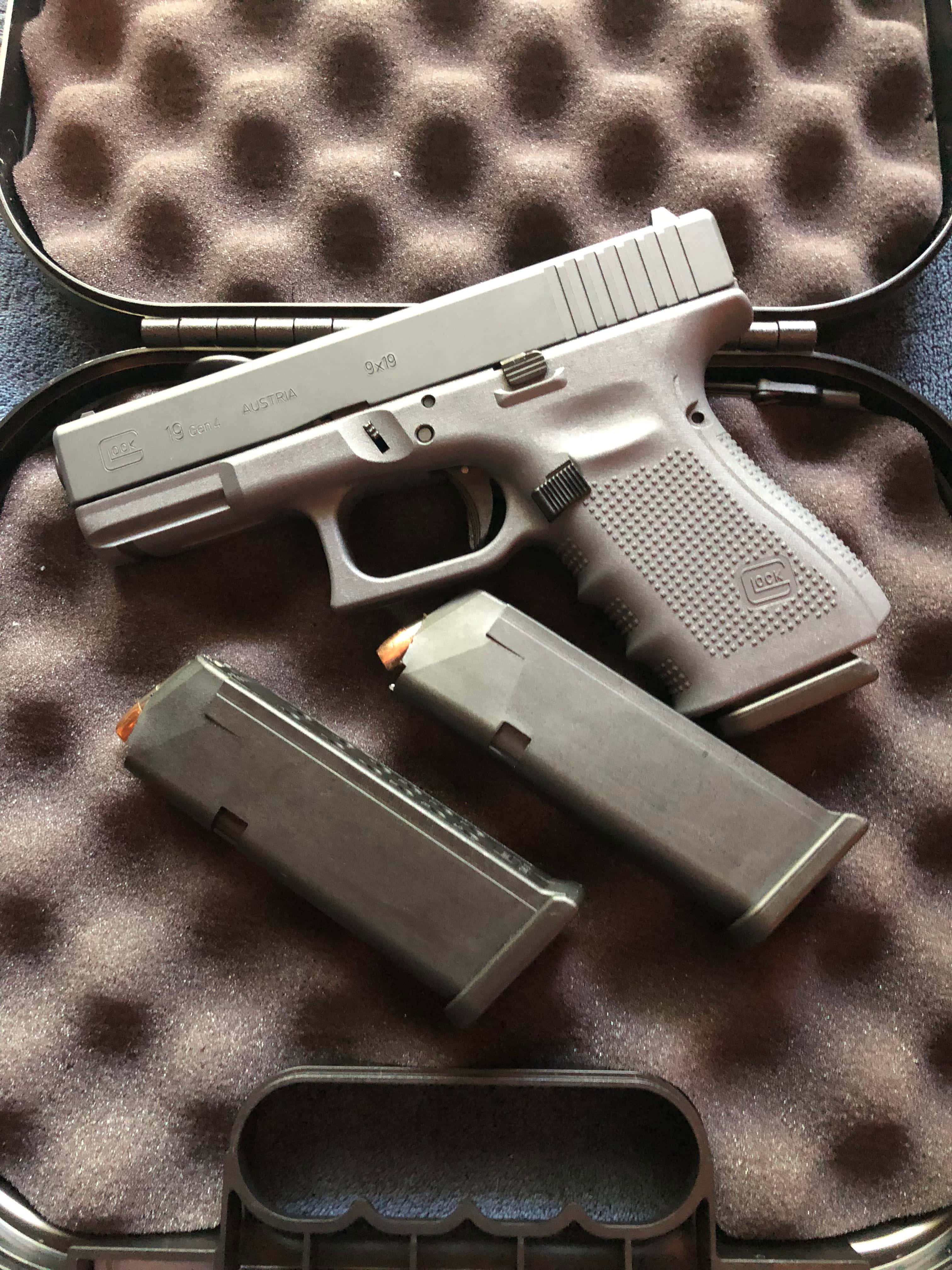 Glock 19 桌布 壁紙 — 一把銀色Glock手槍連同兩個彈匣，在明亮燈光下放置於泡棉內襯的盒子中。