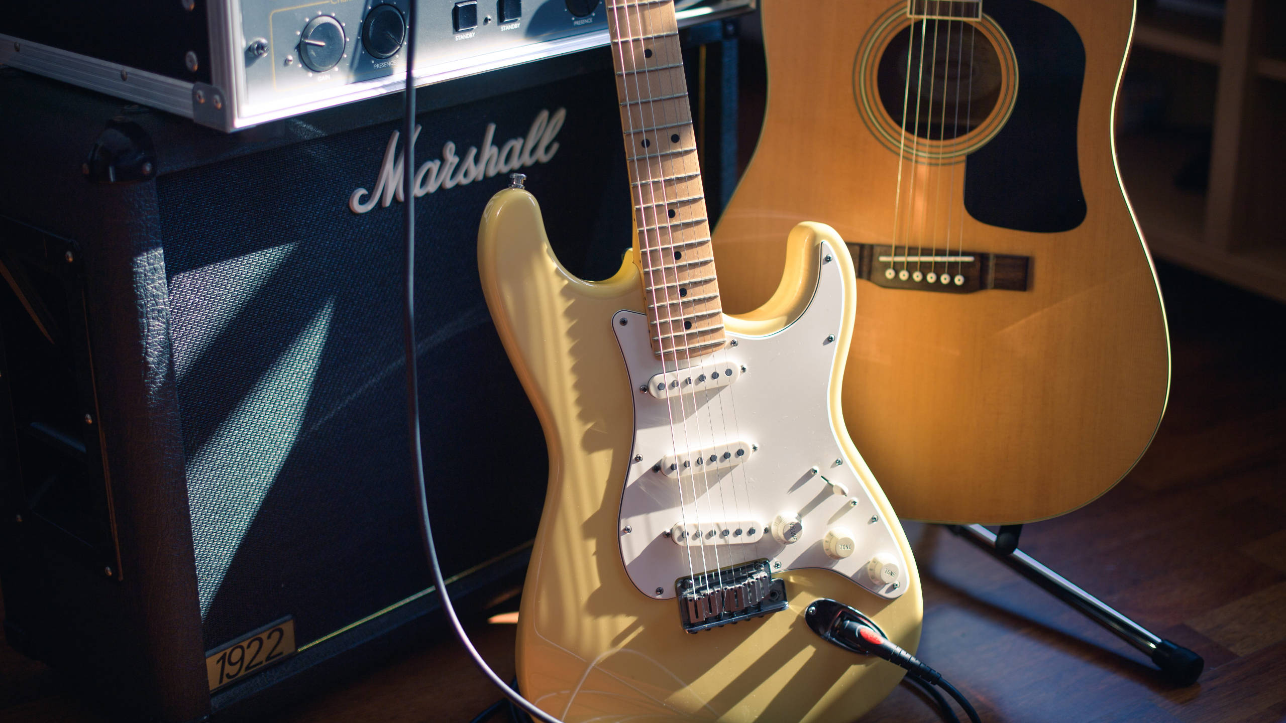 Marshall 桌布 壁紙 — 一把陽光照射的黃色電吉他靠在黑色Marshall擴音機旁，旁邊的吉他架上有一把木吉他。