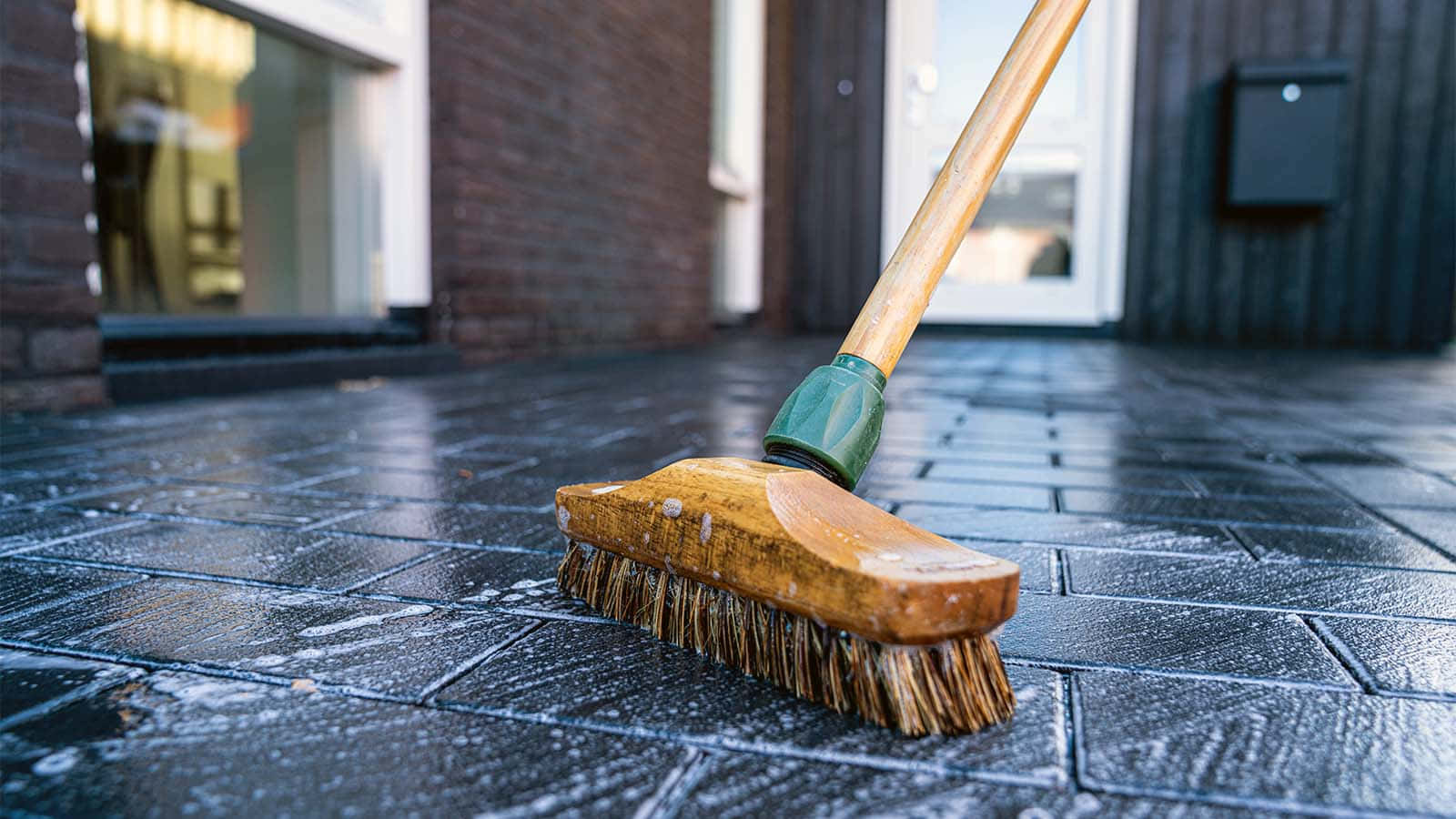 Cleaning 桌布 壁紙 — 一把風化的木掃帚，帶有硬毛，放在磚砌建築外潮濕的深灰色石磚上。