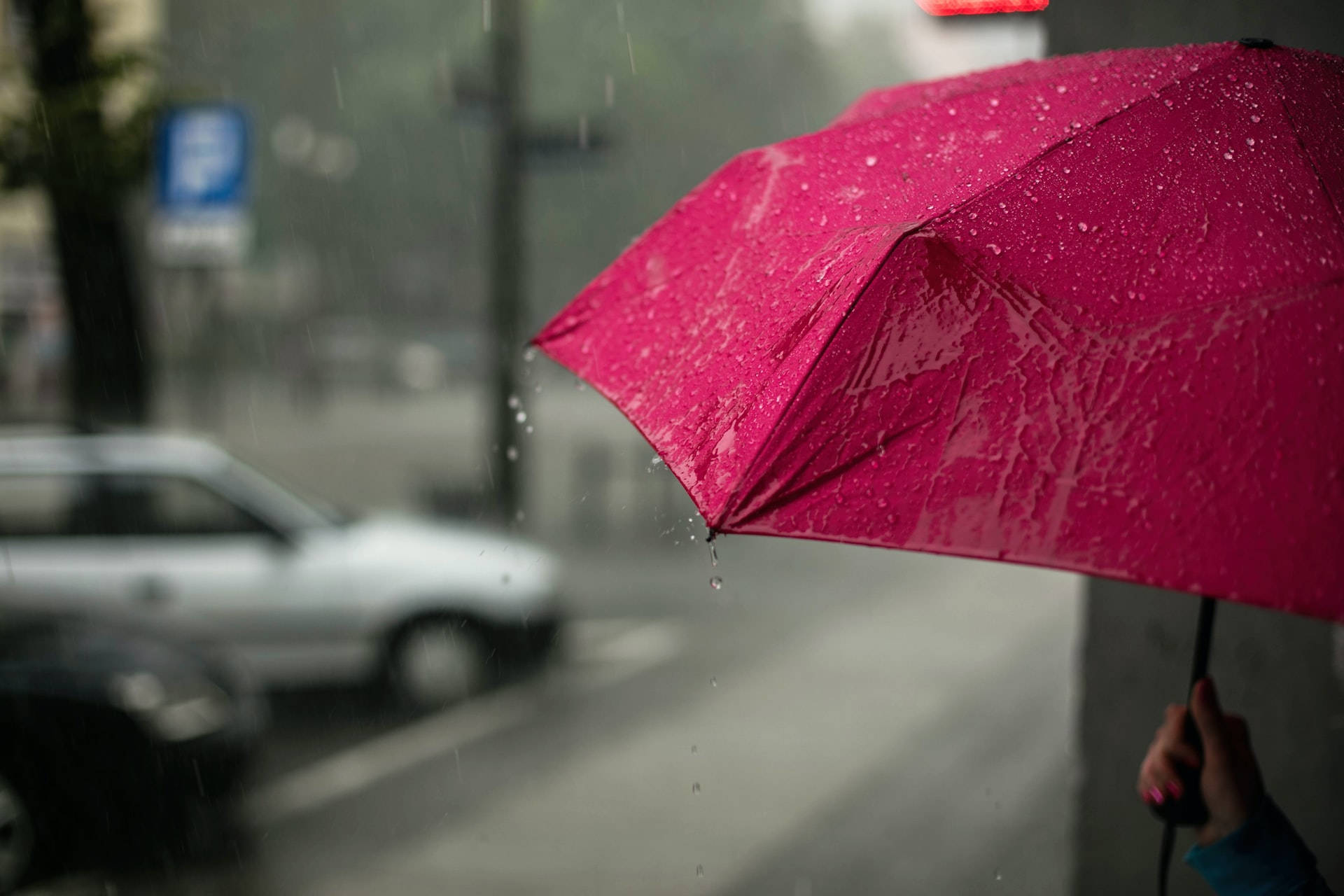 Raining 桌布 壁紙 — 一把鮮豔的粉紅色雨傘在暴雨中，水滴落在模糊的城市街景上。