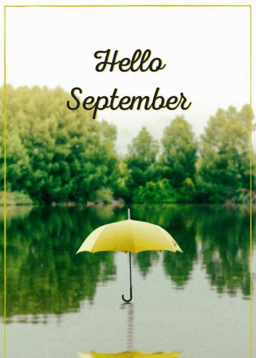 Hello 桌布 壁紙 — 一把鮮黃色的雨傘獨自漂浮在平靜的水面上，映照著綠樹，在柔和的多雲天空下，帶有「Hello September」文字。