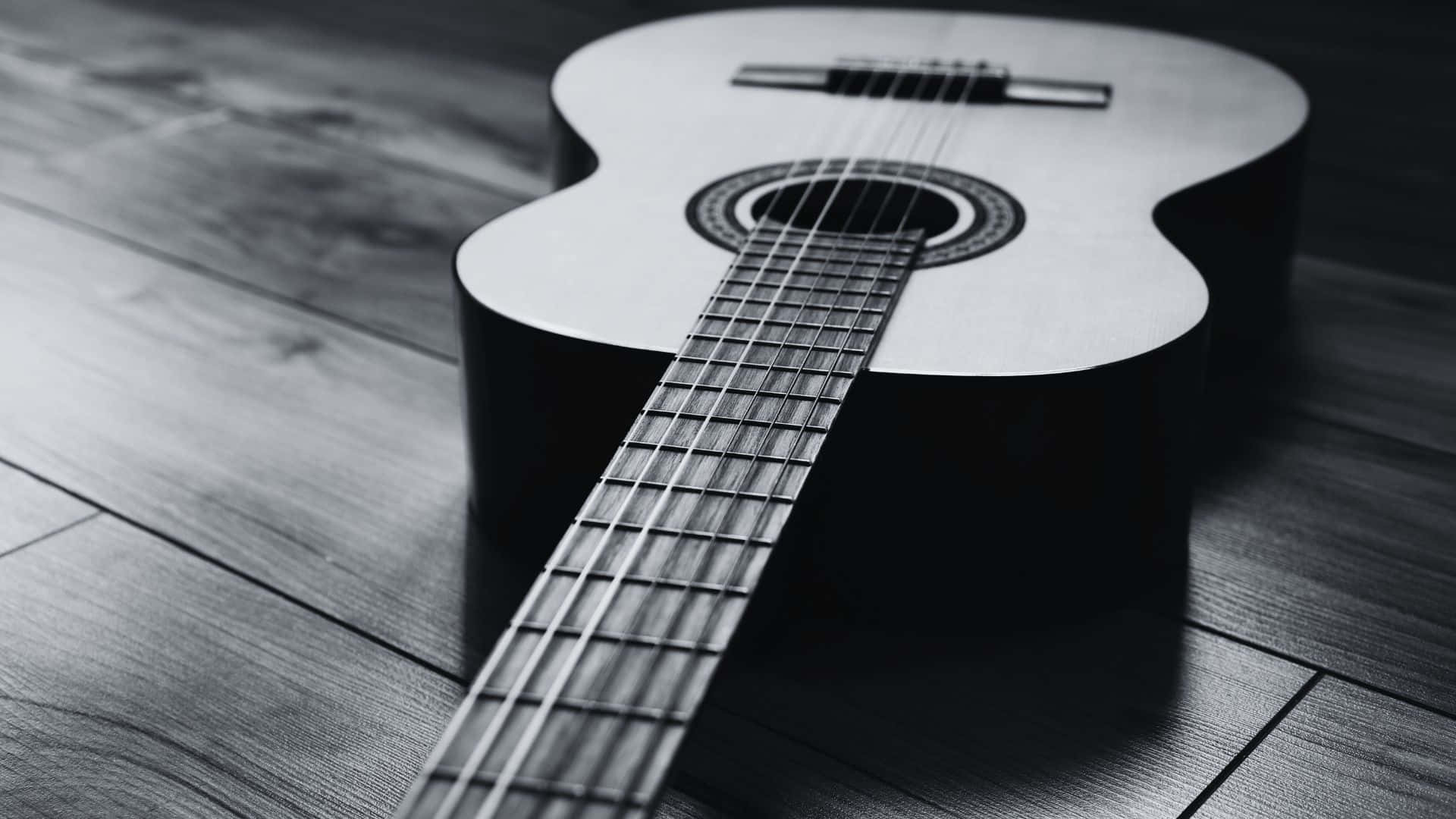 Black And White Guitar 桌布 壁紙 — 一把黑白原聲吉他斜放在木地板上，帶有戲劇性的陰影。