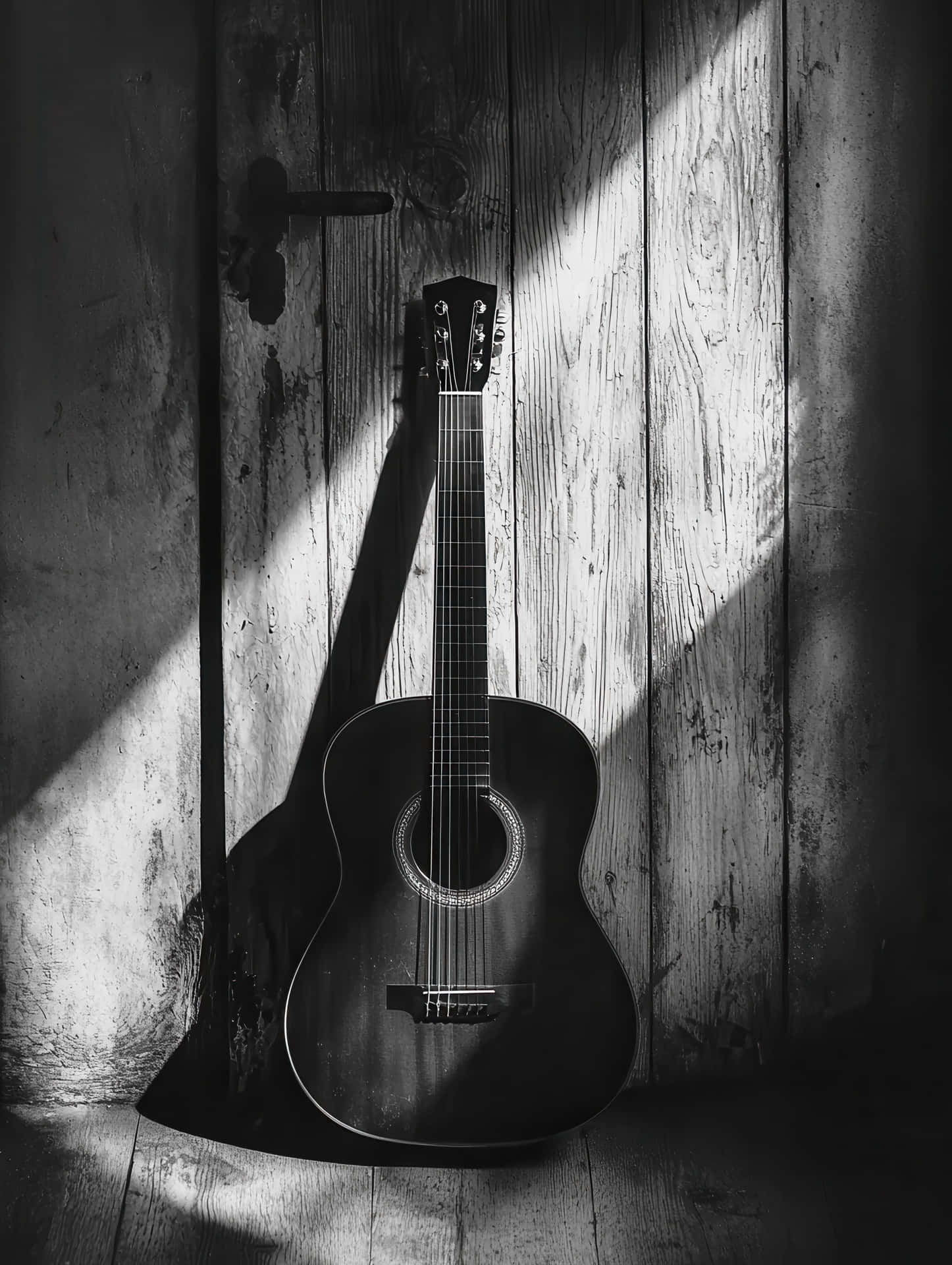 Moody Black and White Acoustic Guitar in Rustic Light 壁紙 — 一把黑白原聲吉他靠在一道飽經風霜的木門上，沐浴在戲劇性的斜陽中。