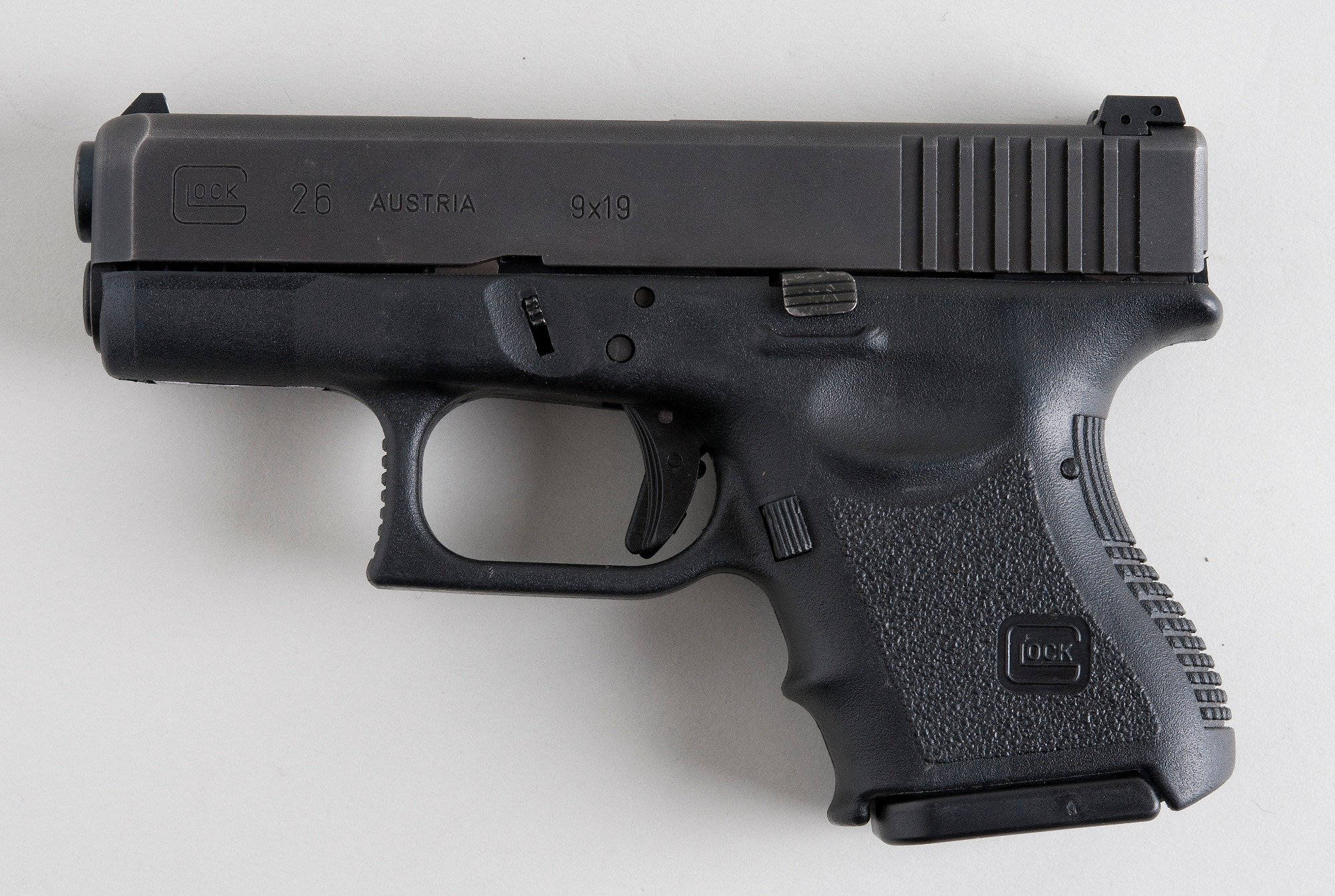 Glock 桌布 壁紙 — 一把黑色 Glock 26 手槍水平放置在純白色表面上，展示其紋理握把和雕刻標記。
