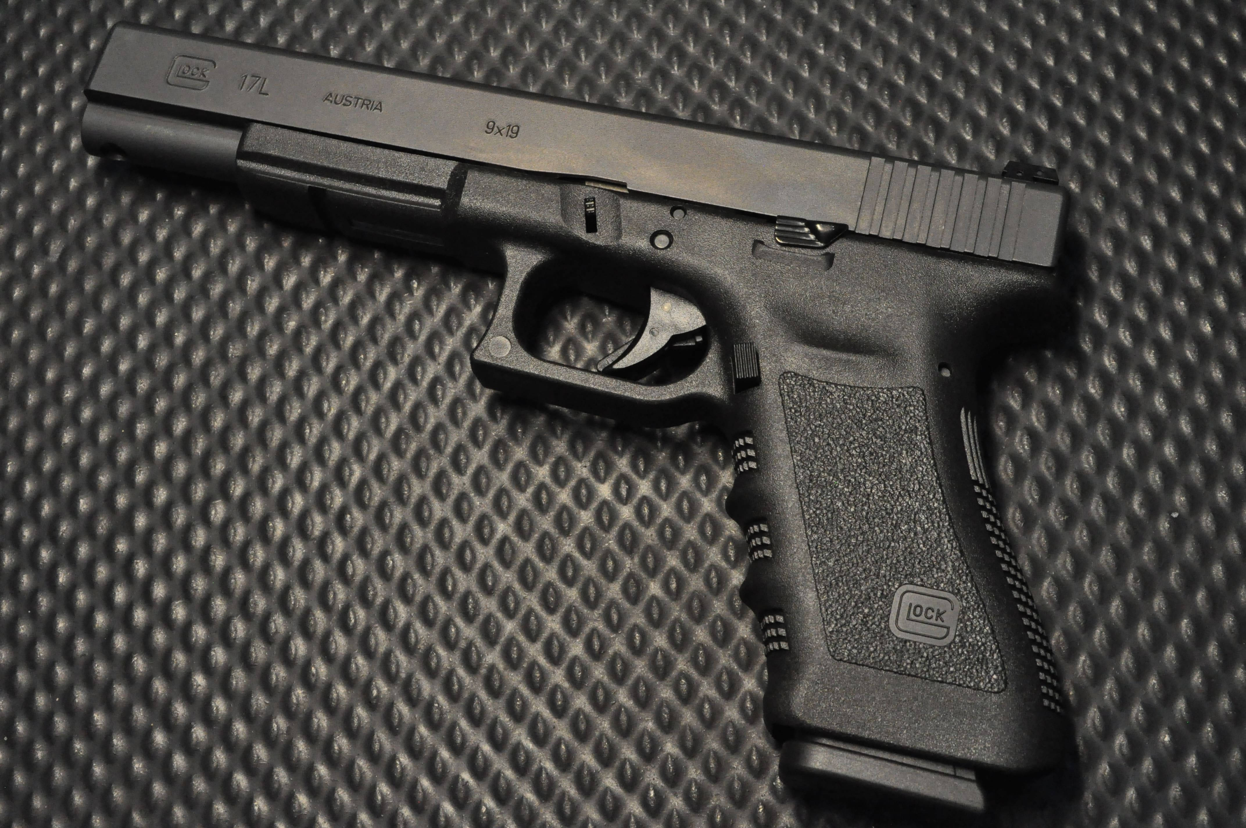 克拉克 桌布 壁紙 — 一把黑色Glock 17L手槍放置在帶紋理的黑色表面上，精確的燈光凸顯其輪廓和雕刻。