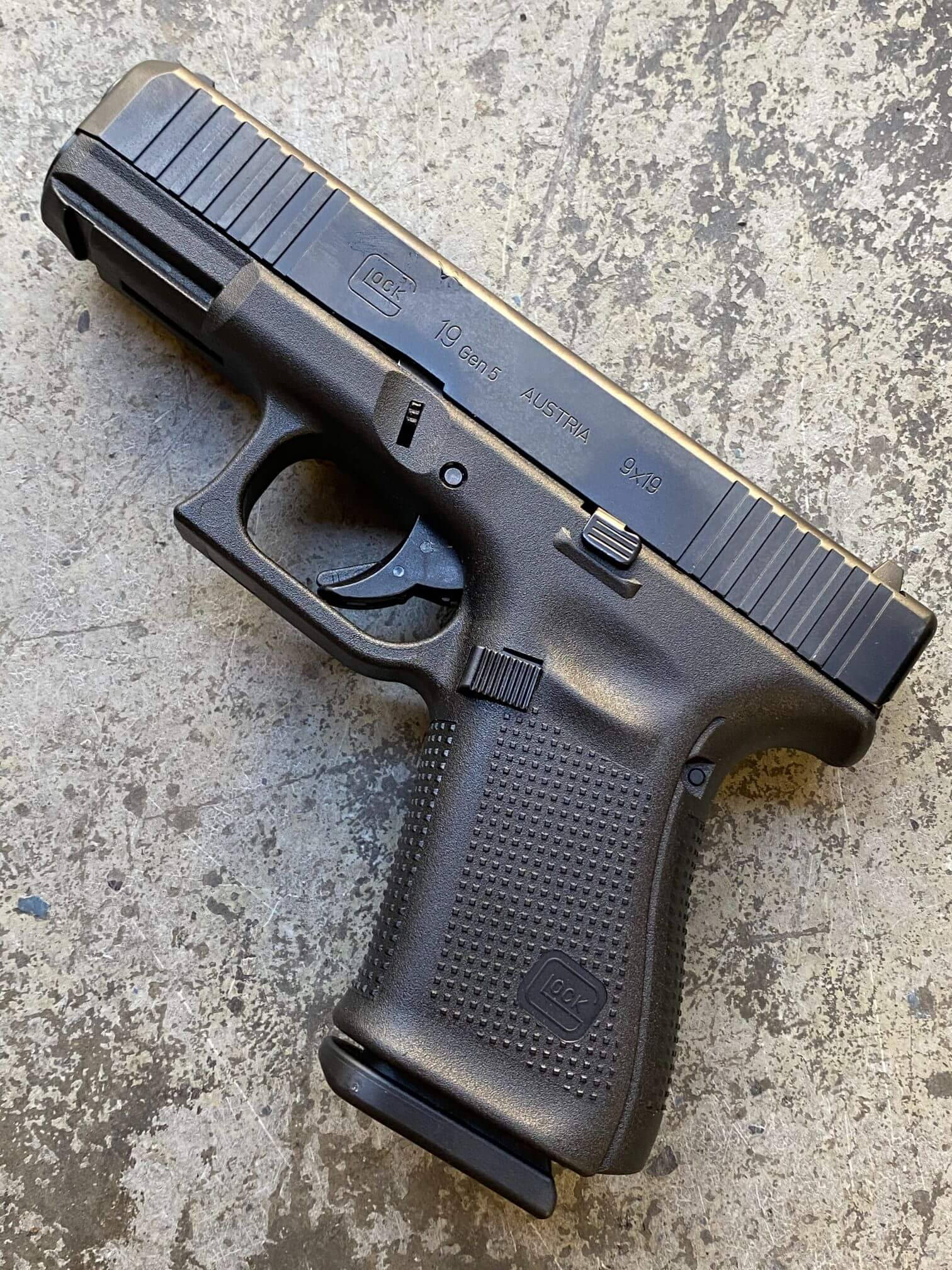 克拉克 桌布 壁紙 — 一把黑色Glock 19 Gen5手槍放在風化的混凝土表面上，有可見的刮痕和污漬。