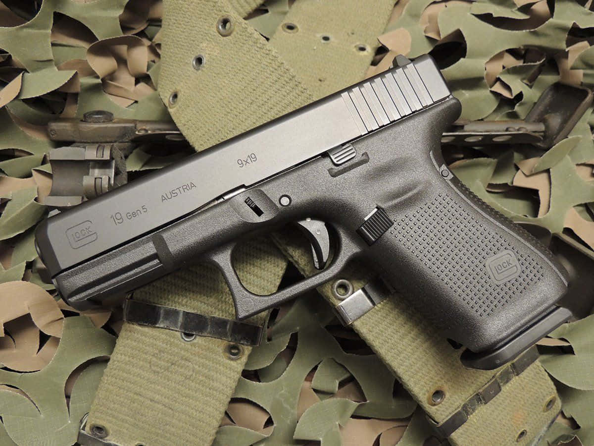 Glock 19 桌布 壁紙 — 一把黑色Glock 19 Gen5手槍放在橄欖綠色迷彩布料上，布料有明顯磨損和縫線。