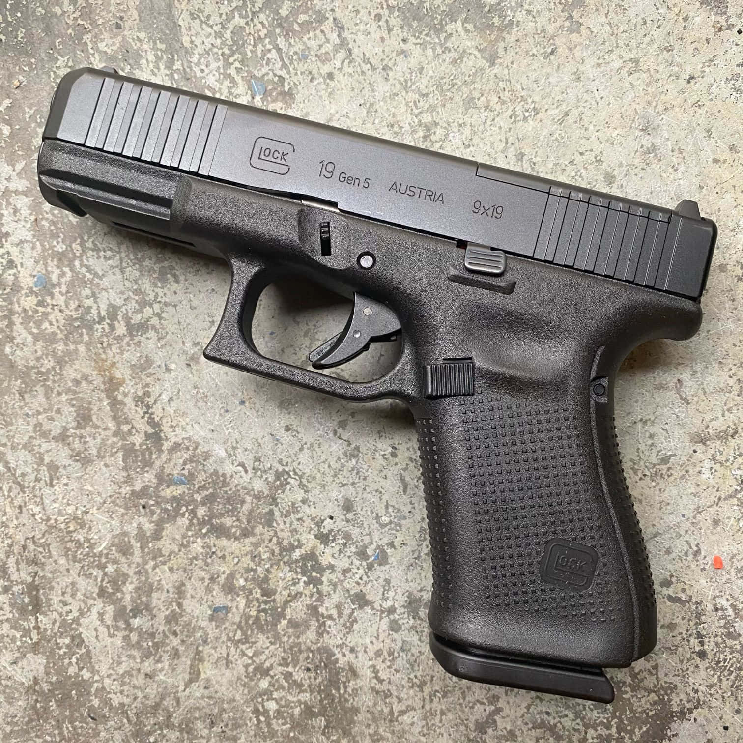 Glock 19 桌布 壁紙 — 一把黑色Glock 19 Gen 5手槍放在有紋理和污漬的風化混凝土表面上。