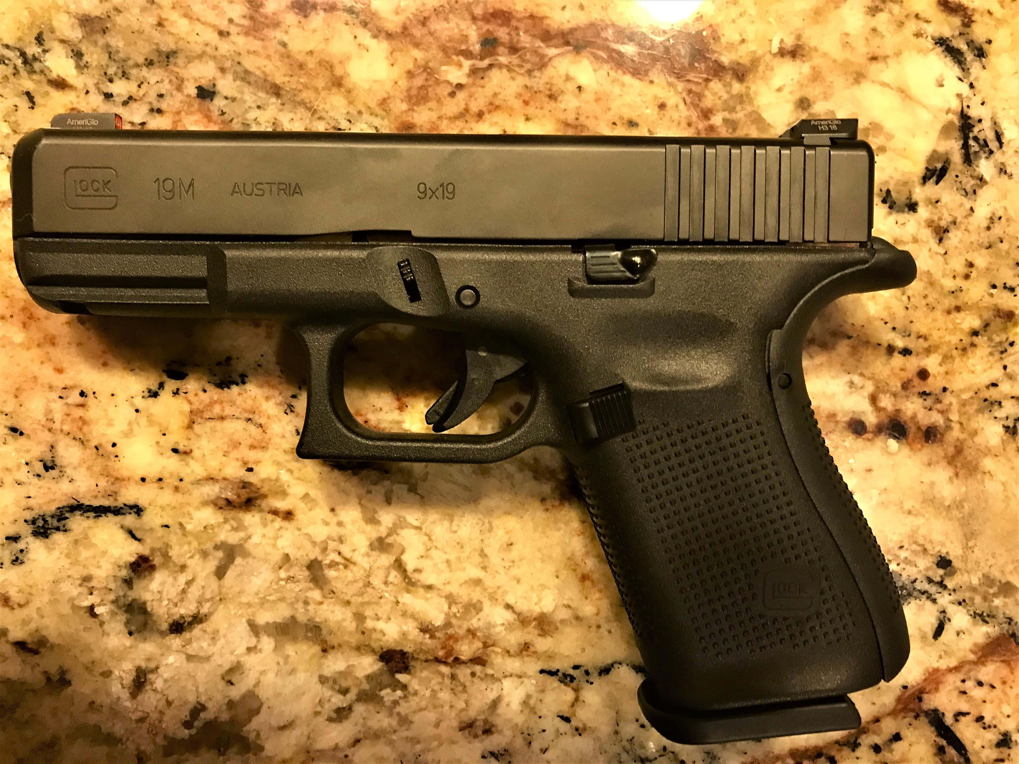 Glock 19 桌布 壁紙 — 一把黑色Glock 19M手槍放在有斑點的米色檯面上，處於溫暖的室內燈光下。