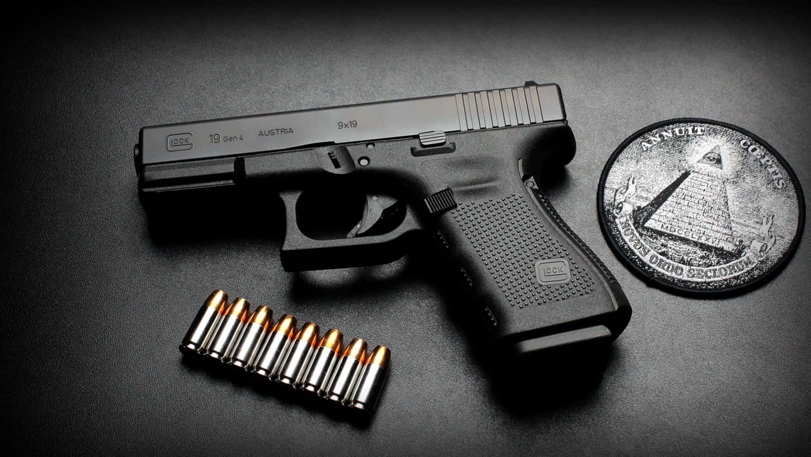 Glock 19 桌布 壁紙 — 一把黑色Glock 19手槍、九發9x19mm子彈和一枚共濟會硬幣放在深色紋理表面上，在戲劇性的燈光下。
