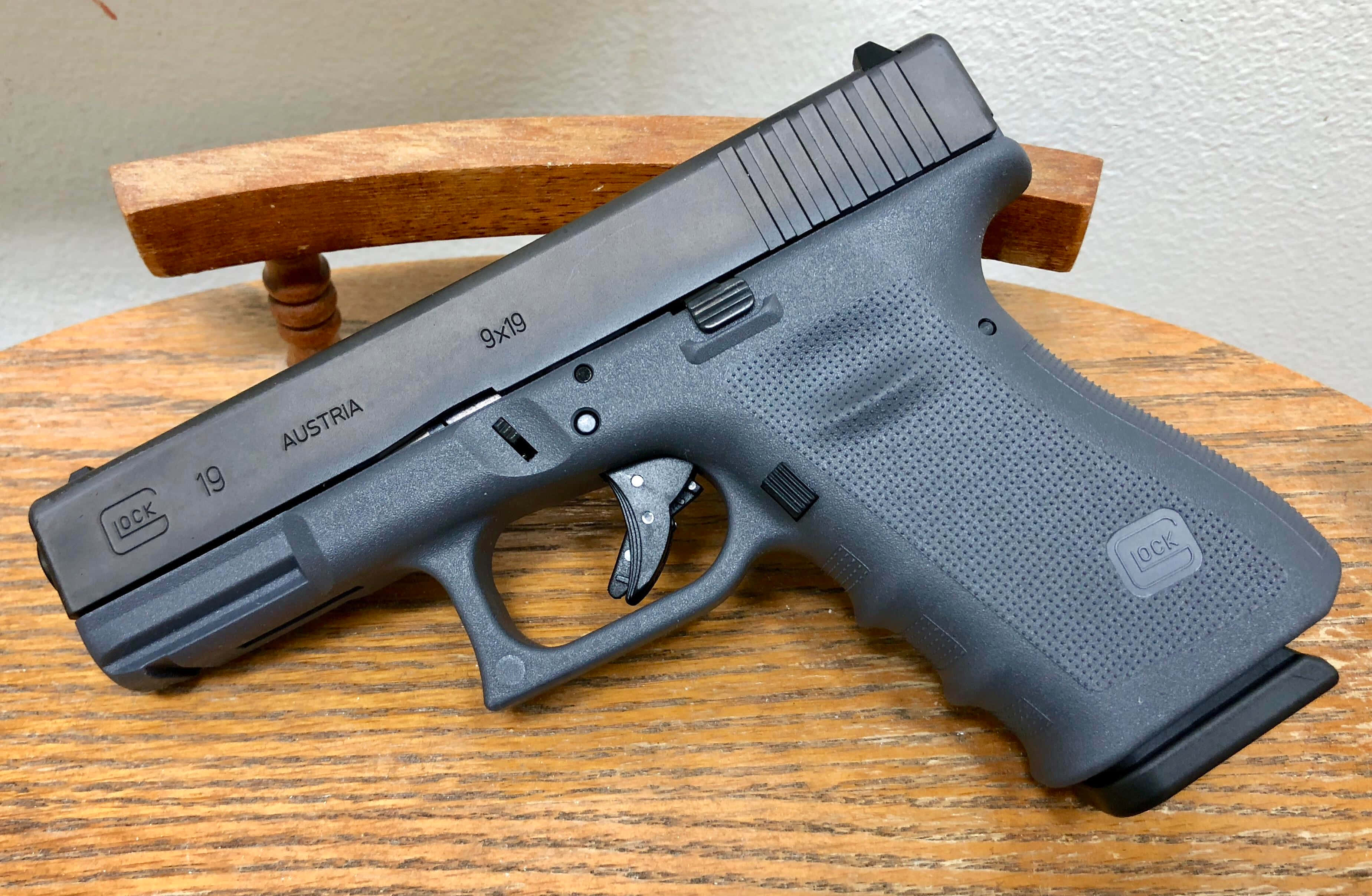 Glock 19 桌布 壁紙 — 一把黑色Glock 19手槍放在木桌上，帶有紋理握把和可見標記。
