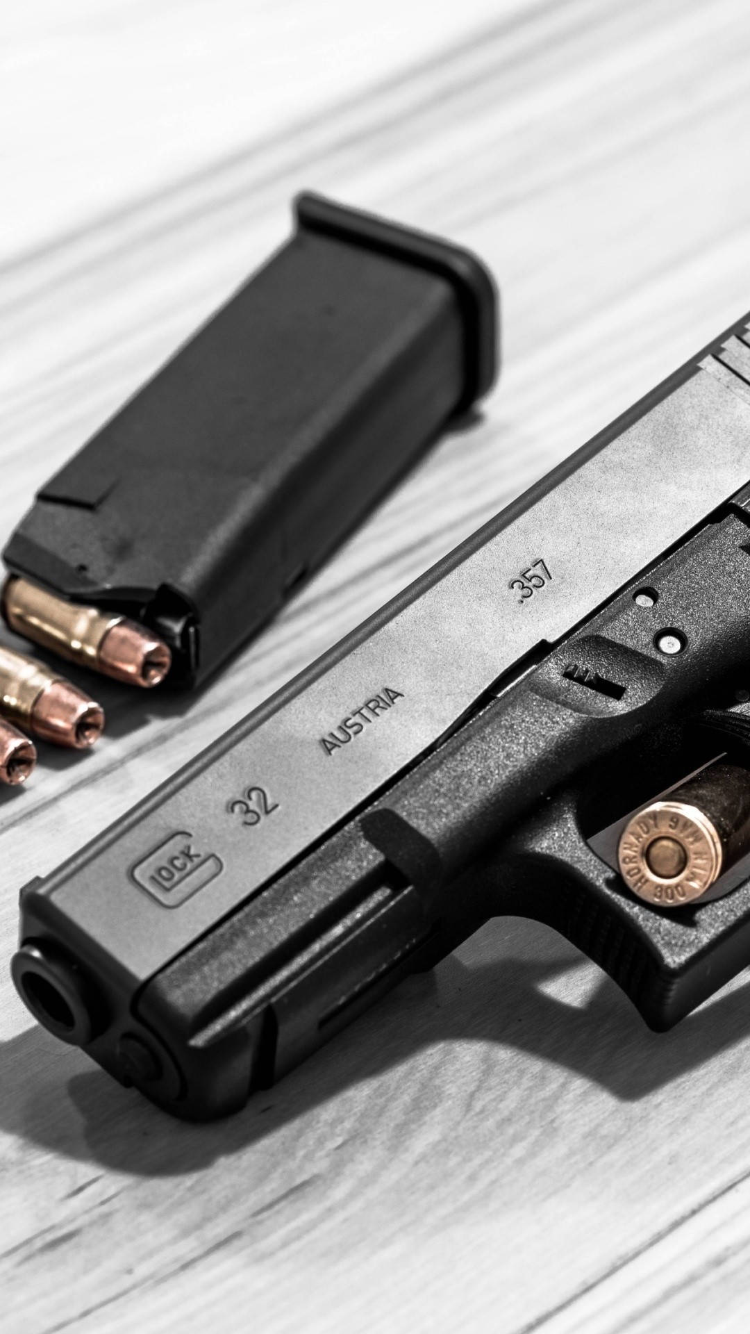 Glock 桌布 壁紙 — 一把黑色Glock 32手槍連彈匣及銅包子彈放在淺色木質表面上，呈現高對比黑白效果。