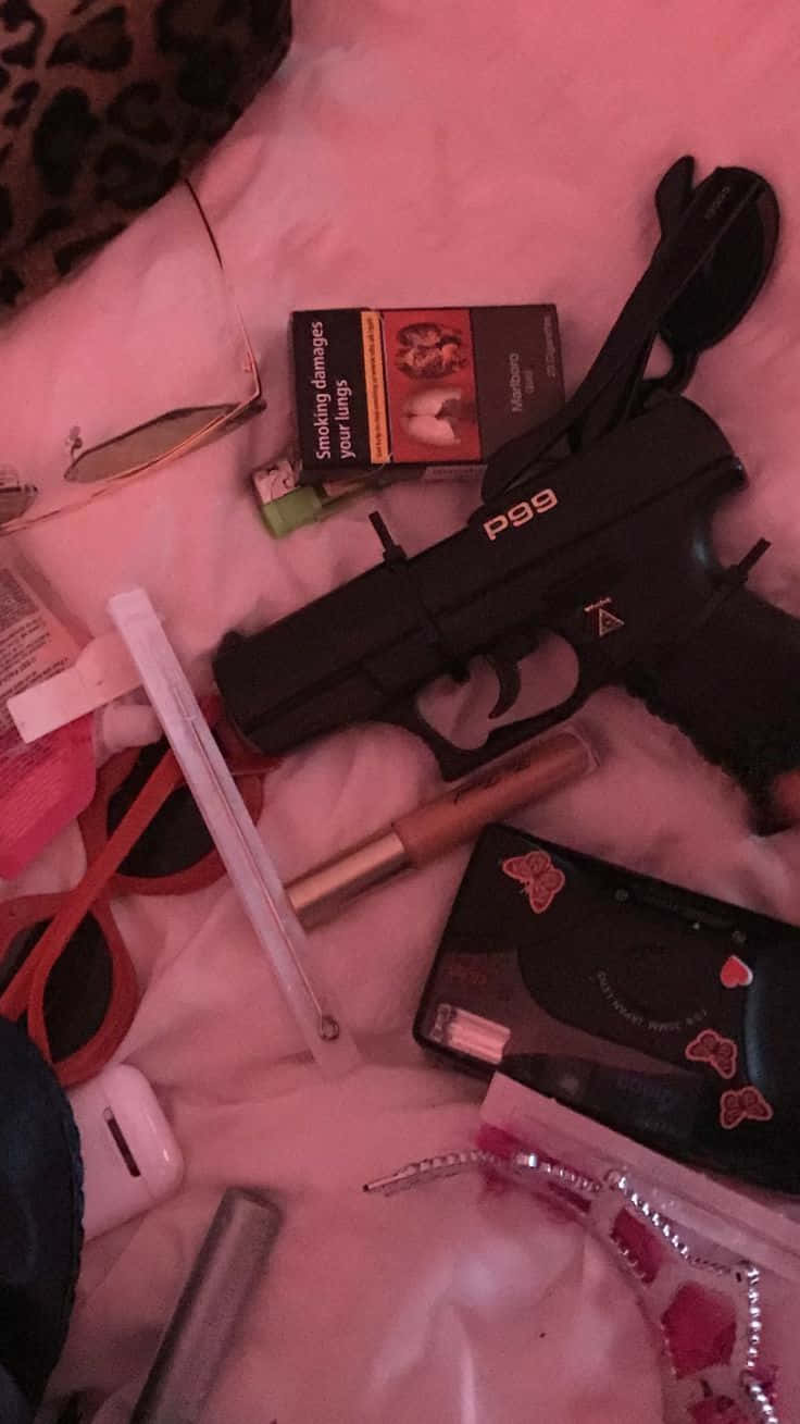 Boujee 桌布 壁紙 — 一把黑色P99手槍放在化妝品、香煙和個人物品之間，置於粉紅色毯子上，在昏暗的紅光下。