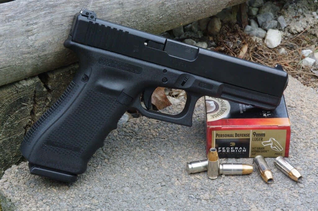 bullet 桌布 壁紙 — 一把黑色半自動手槍放在一盒9mm子彈上，旁邊有散落的子彈，置於岩石戶外表面。