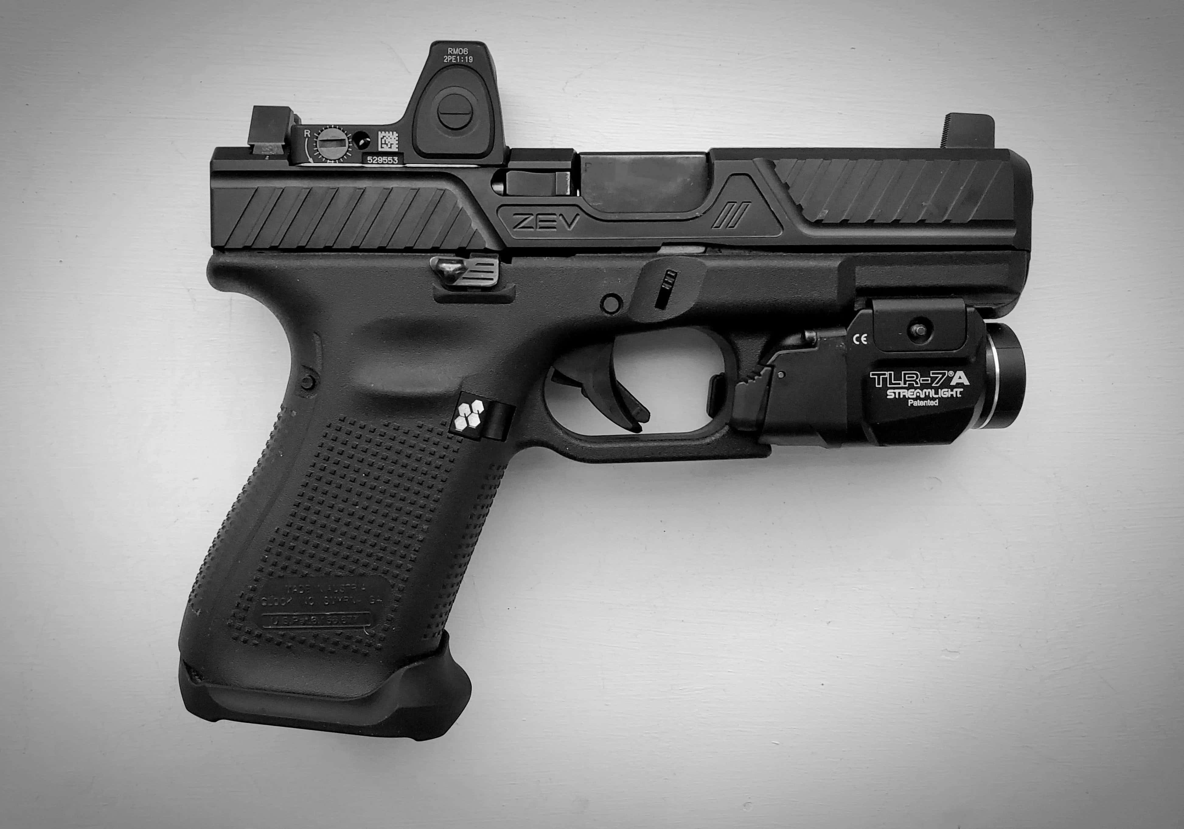 Glock 19 桌布 壁紙 — 一把黑色半自動手槍配備紅點瞄準器和戰術燈，放置在純灰色表面上。