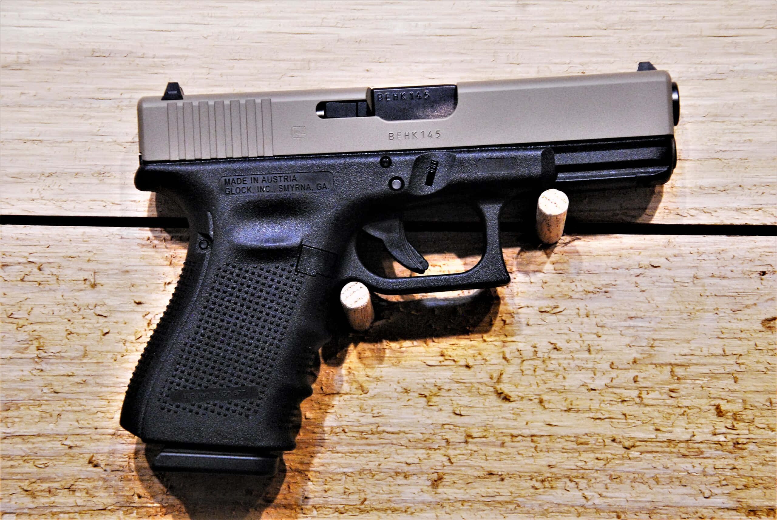 Glock 19 桌布 壁紙 — 一把黑色和銀色的Glock手槍放在淺色木質表面上，附近有兩顆子彈。