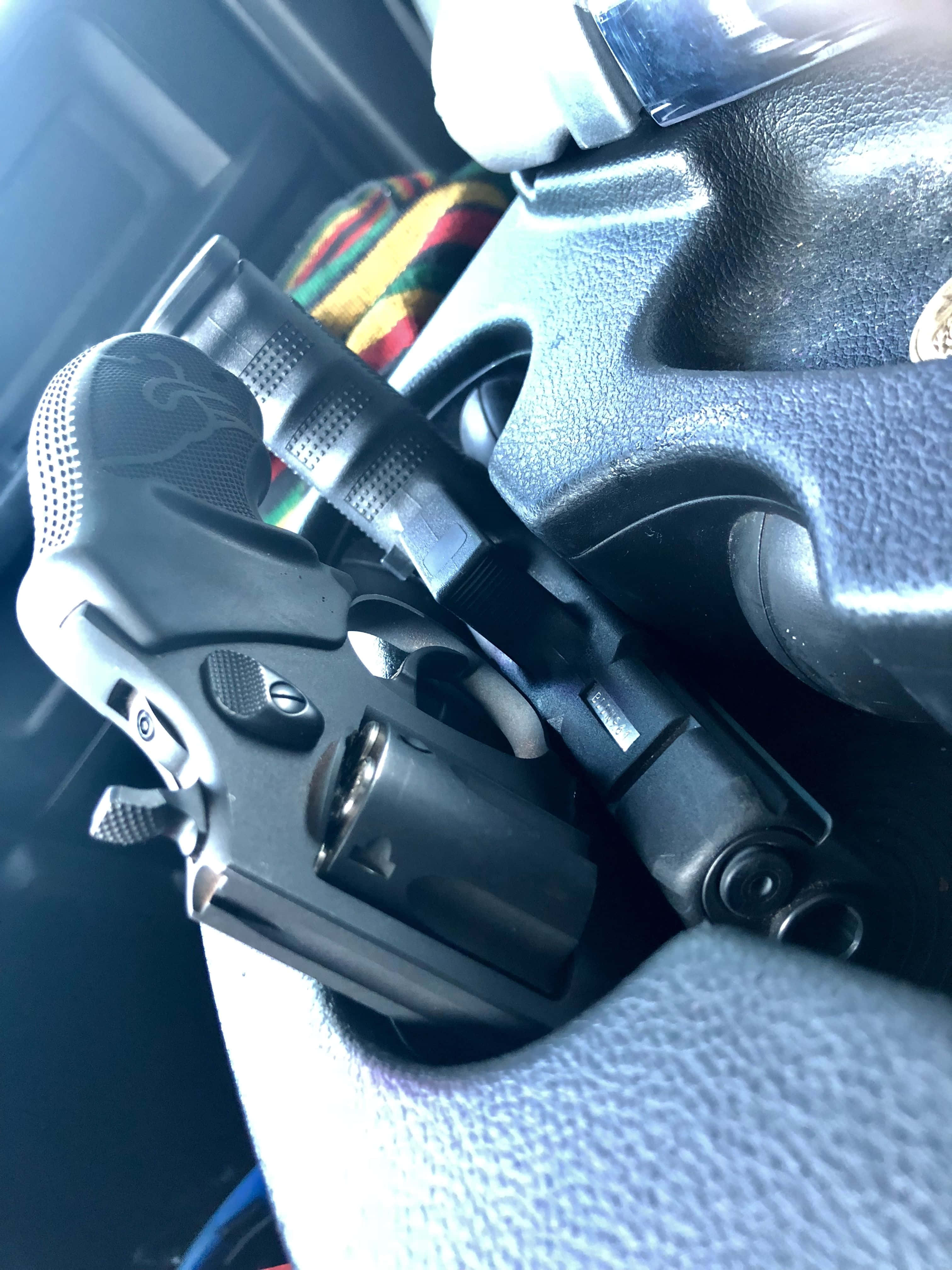 槍枝 桌布 壁紙 — 一把黑色左輪手槍的特寫，放在汽車有紋理的方向盤上，背景有一塊色彩繽紛的布。