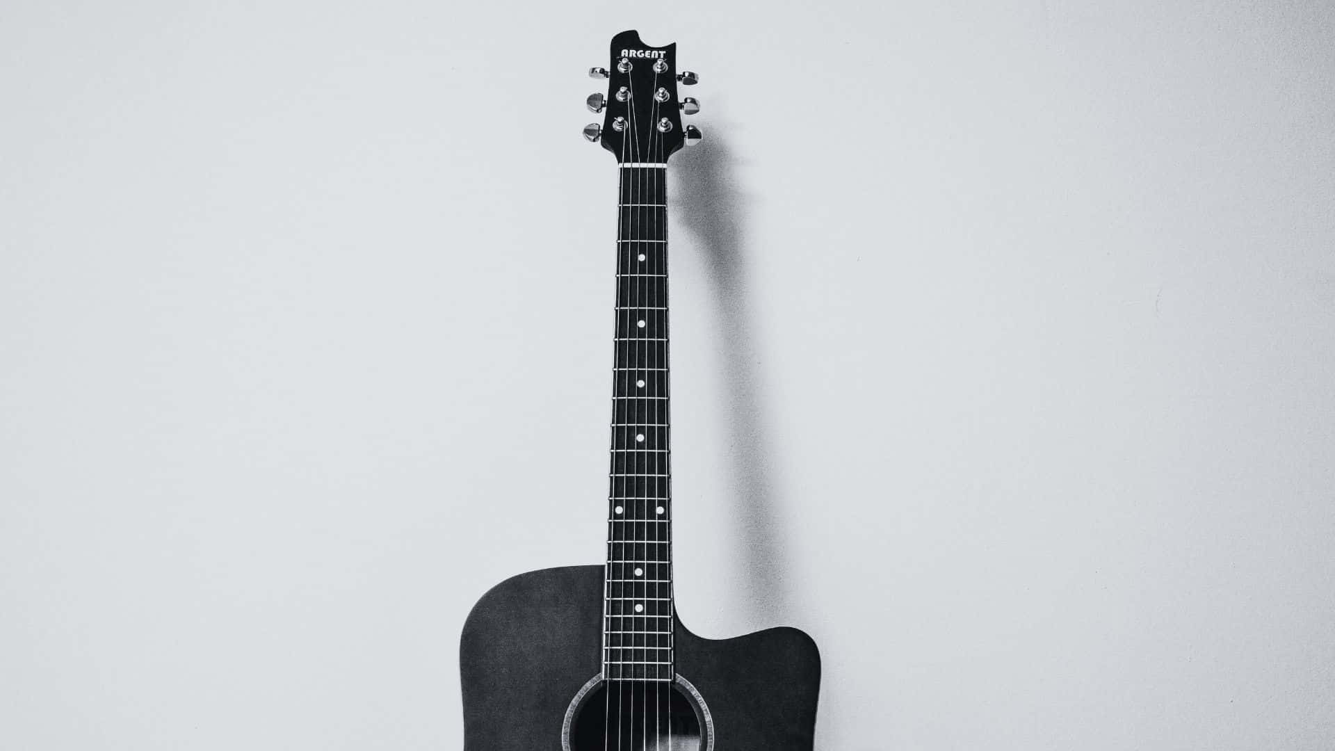 Black And White Guitar 桌布 壁紙 — 一把黑色木吉他垂直掛在純淺灰色牆上，投下柔和陰影。