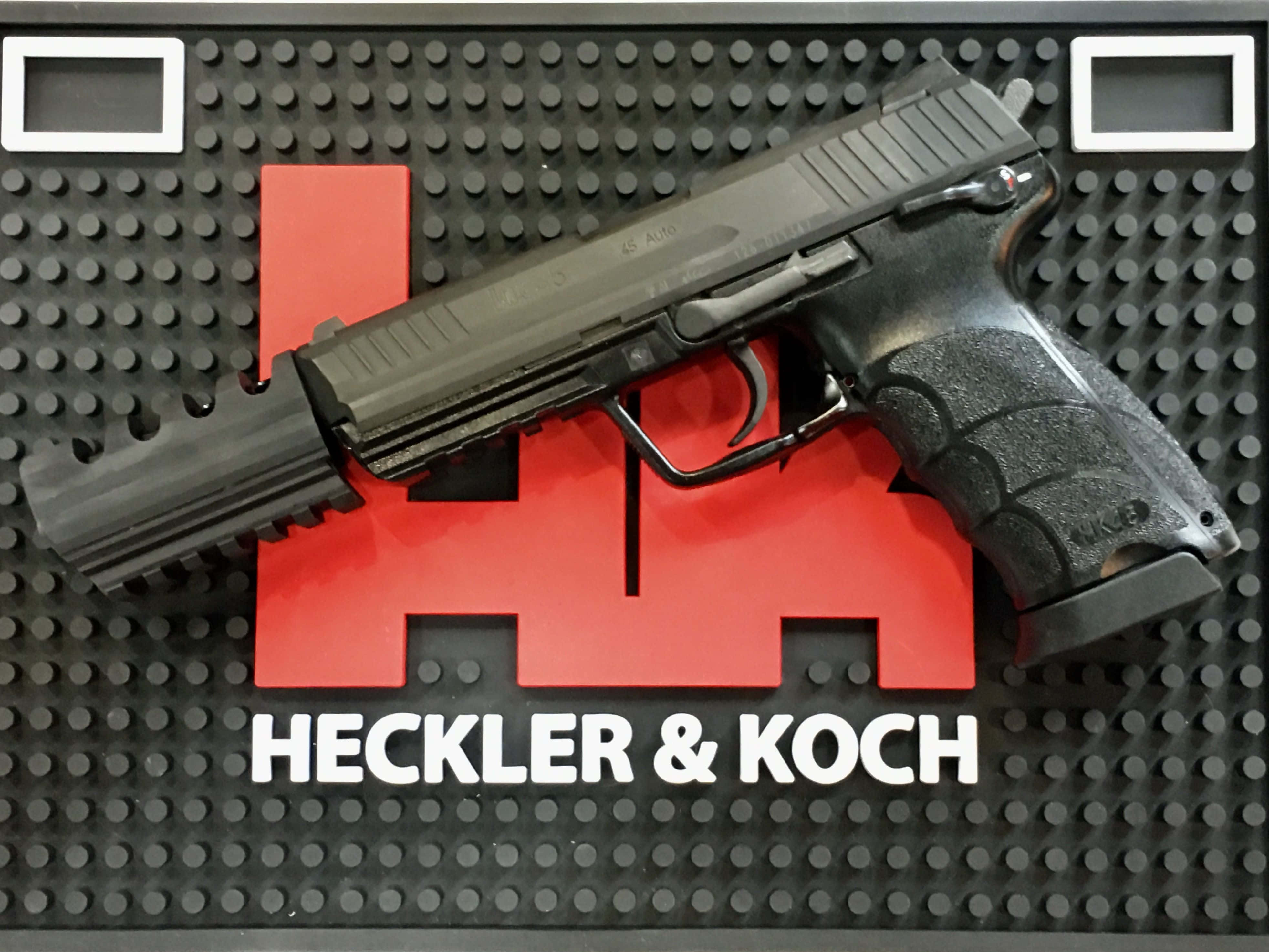 槍枝 桌布 壁紙 — 一把黑色的Heckler & Koch手槍放在一個帶有紅色標誌和白色文字的黑色掛板上。