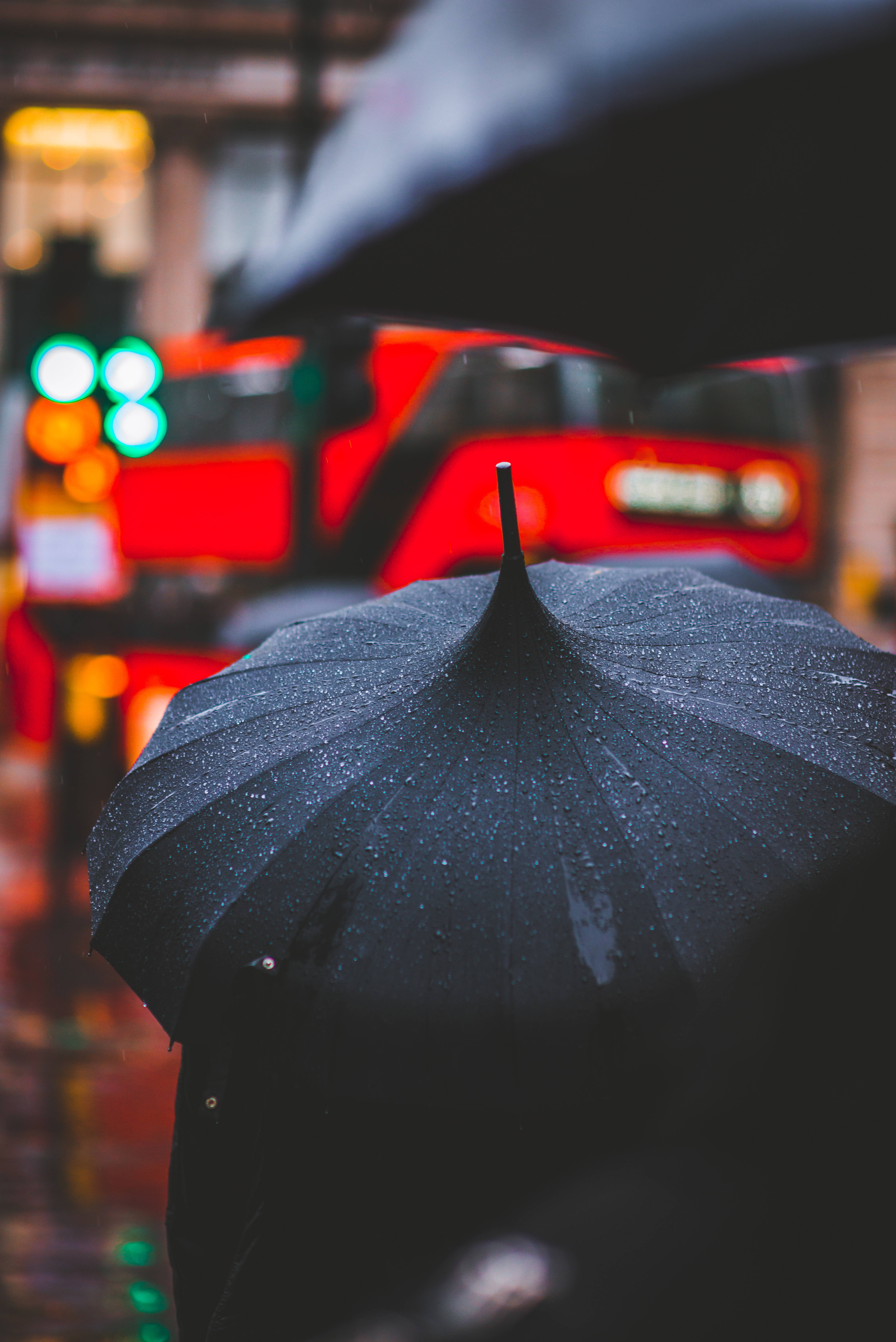下雨 桌布 壁紙 — 一把黑色雨傘上點綴著雨滴，保護著一個人在夜晚穿過霓虹燈閃爍的雨街。