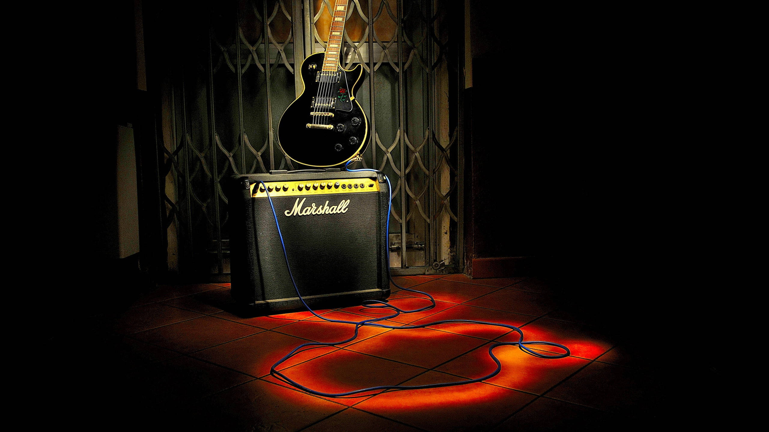 Marshall 桌布 壁紙 — 一把黑色電吉他掛在Marshall音箱上方，在昏暗的房間中，溫暖的橙色光線照射在瓷磚地板上。
