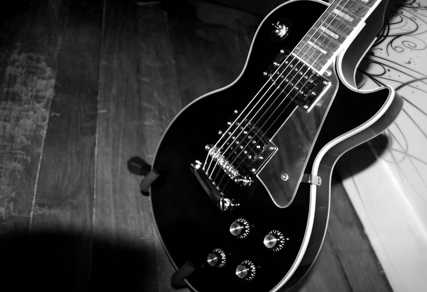 Guitar Aesthetic 桌布 壁紙 — 一把黑色電吉他斜放在木地板上，呈現戲劇性的陰影和高對比度。