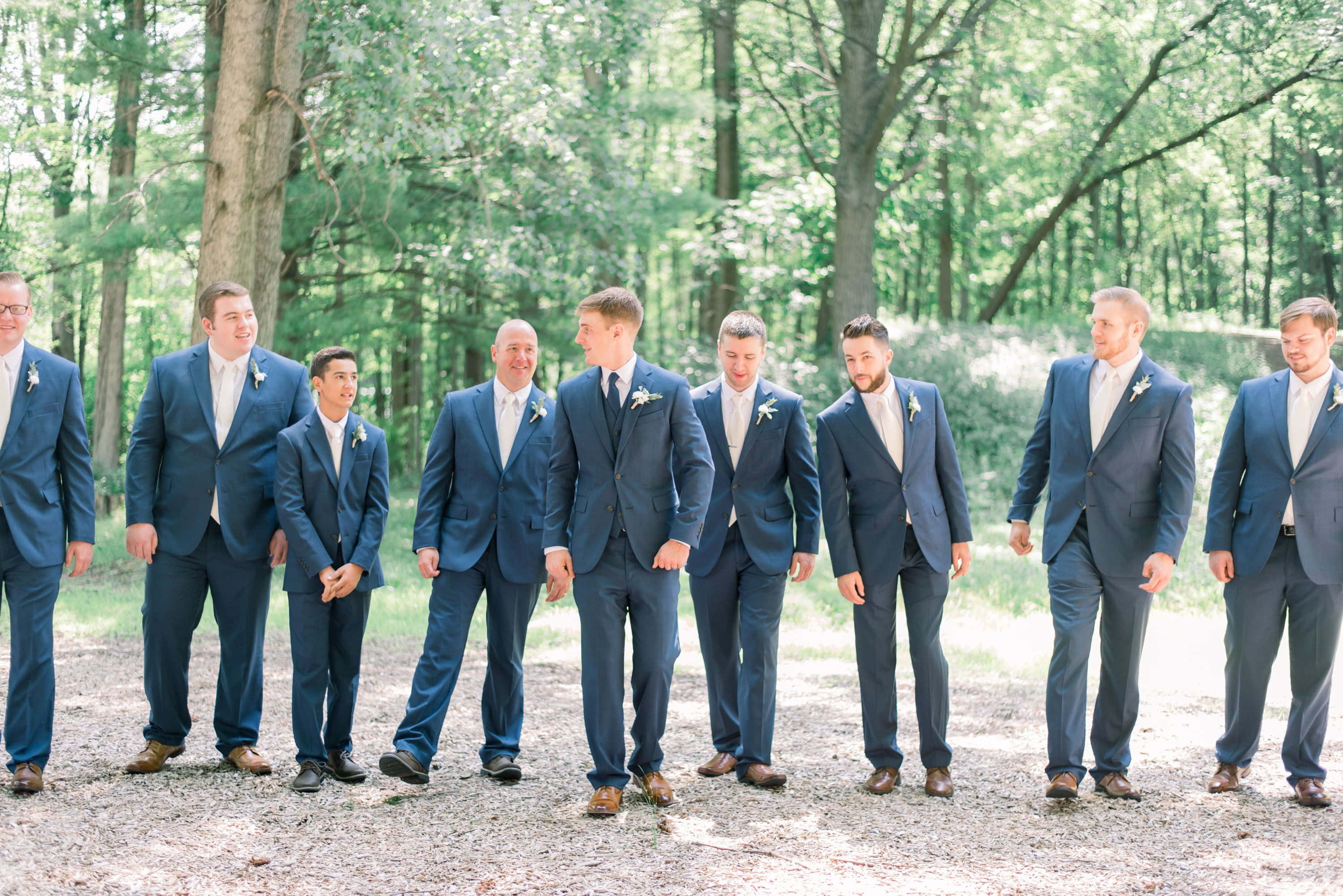 Groomsmen 桌布 壁紙 — 一排伴郎穿著相配的海軍藍西裝，在陽光明媚的森林空地上微笑站立。