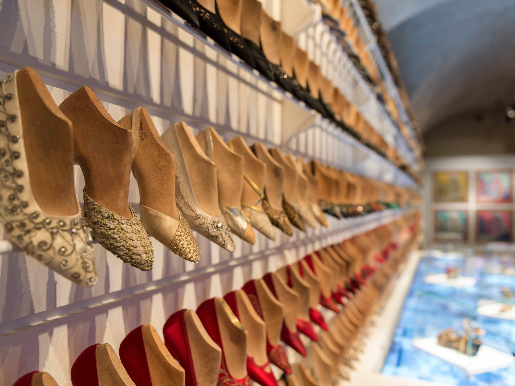 Ferragamo 桌布 壁紙 — 一排優雅的高跟鞋，有米色、紅色和金色，整齊地掛在豪華精品店的白色架子上。