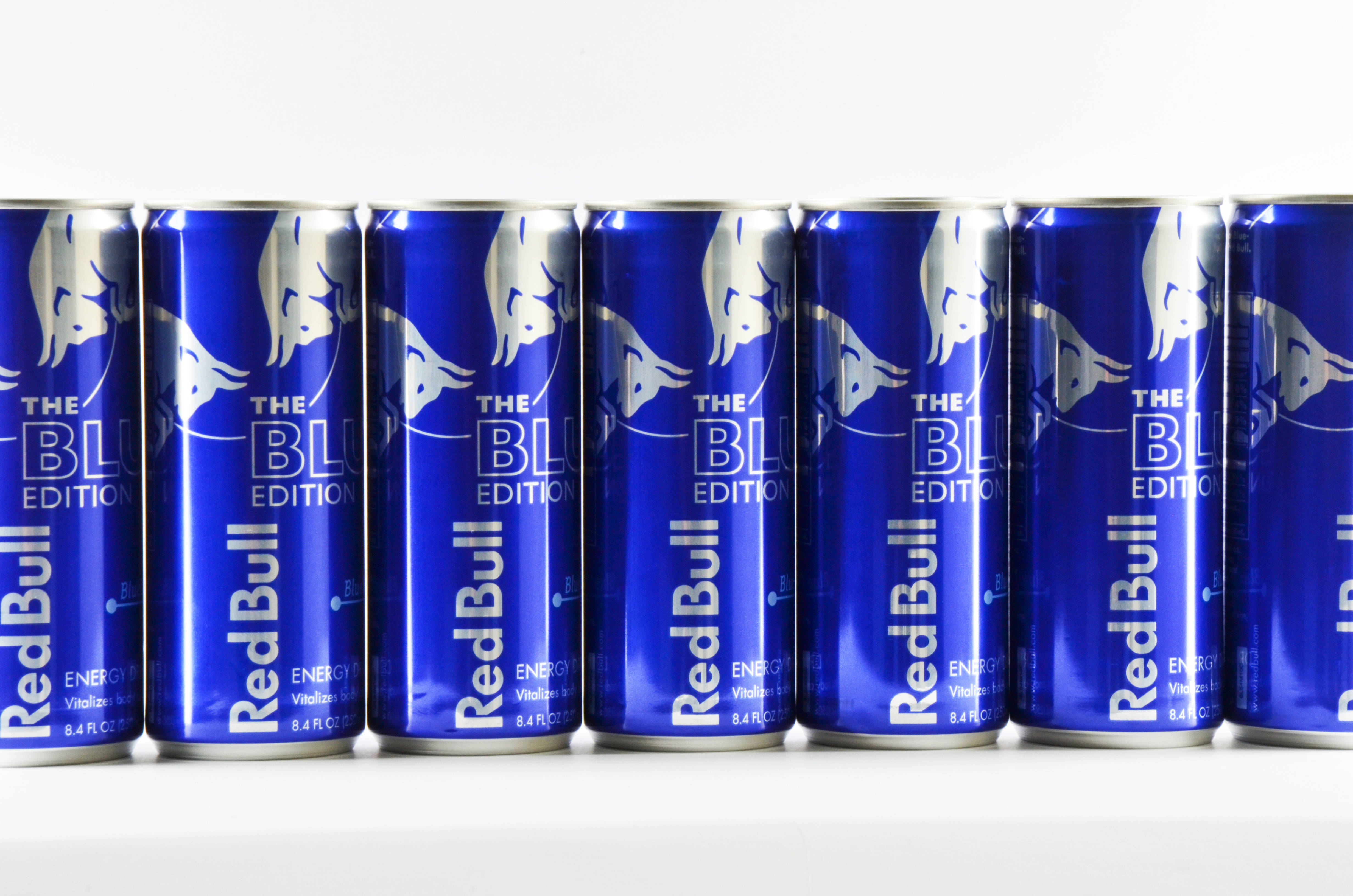 bull 桌布 壁紙 — 一排充滿活力的藍色Red Bull The Blue Edition罐整齊地排列在乾淨的白色背景上。