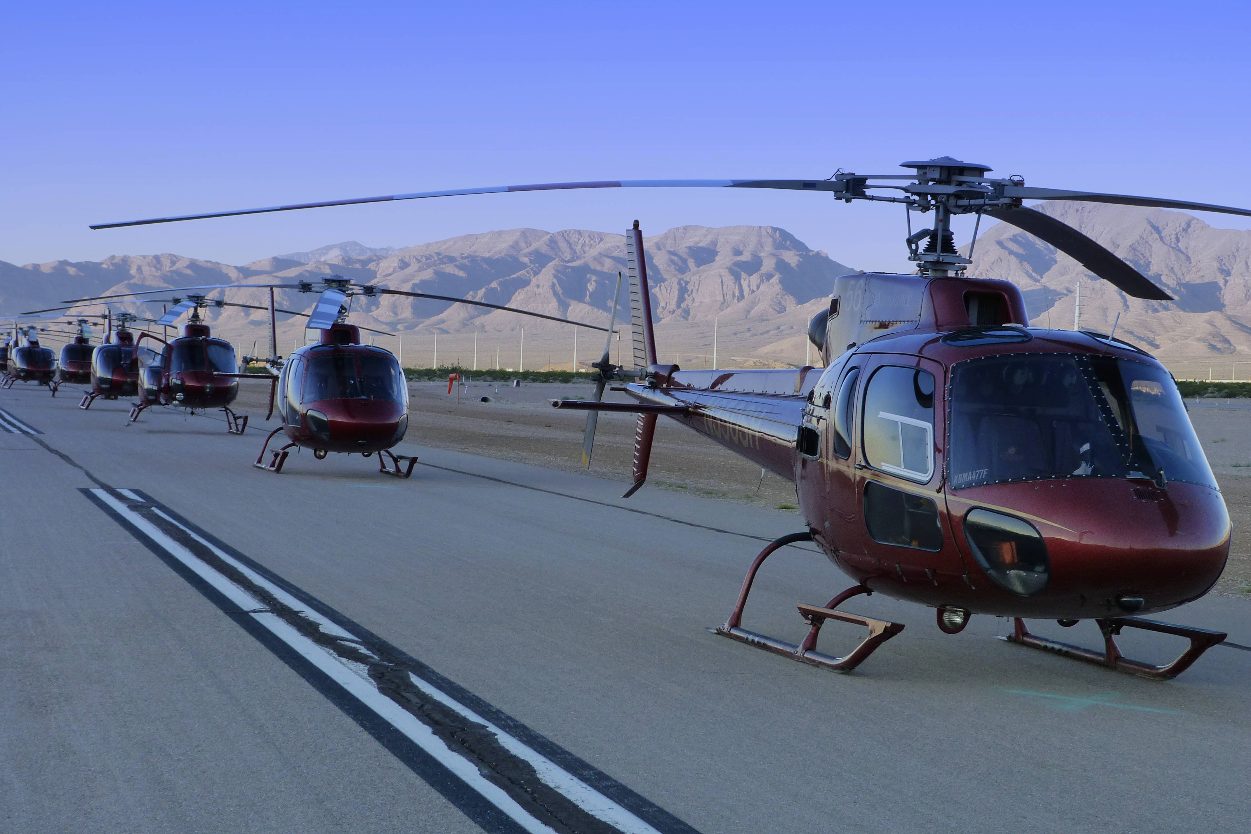 Helicopter 桌布 壁紙 — 一排光亮的紅色直升機停泊在停機坪上，乾旱的山脈在清澈的藍天下聳立。