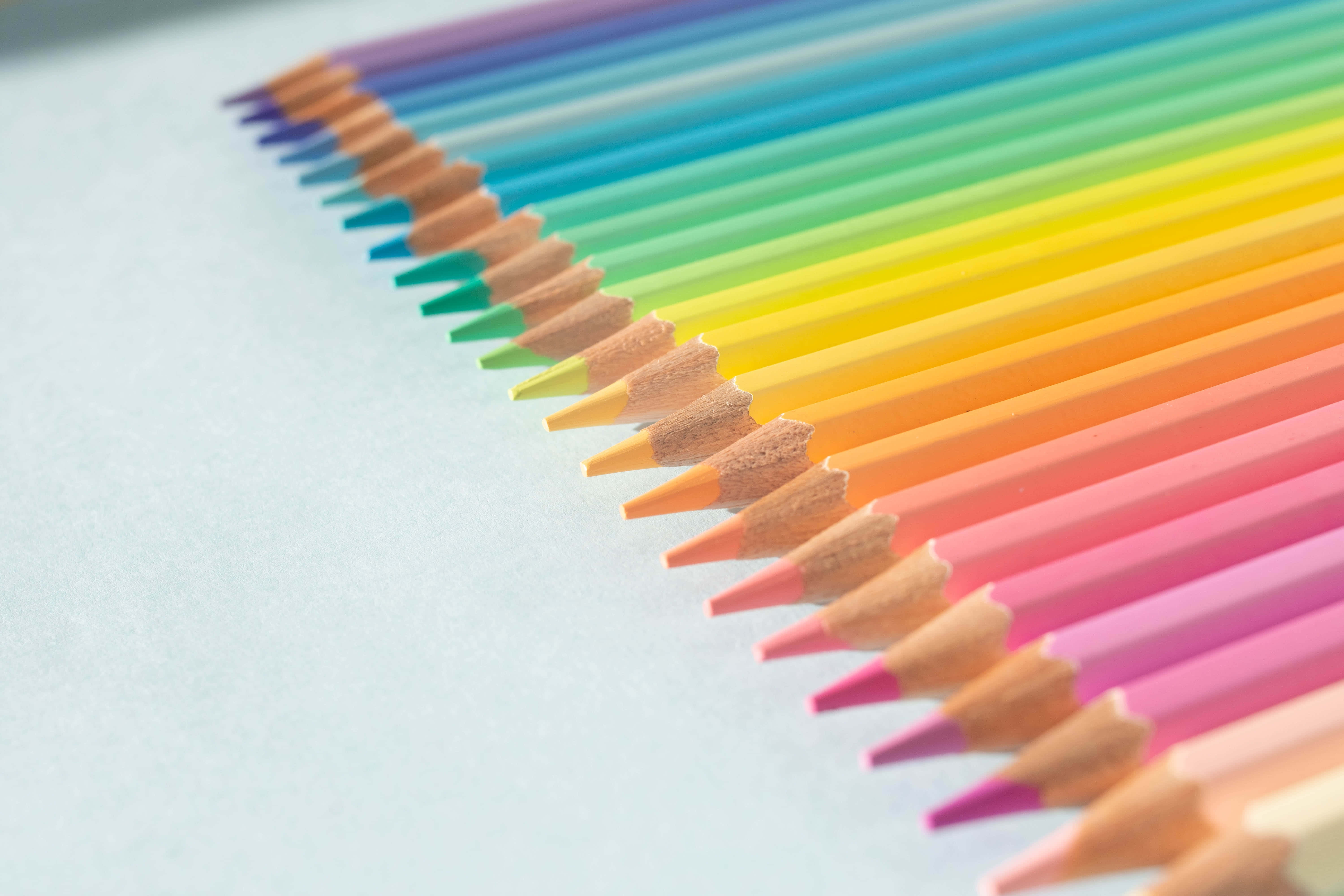 Cute Rainbow Pastel 桌布 壁紙 — 一排削尖的彩色鉛筆以對角線彩虹排列，放置在柔軟的藍色表面上，景深較淺。