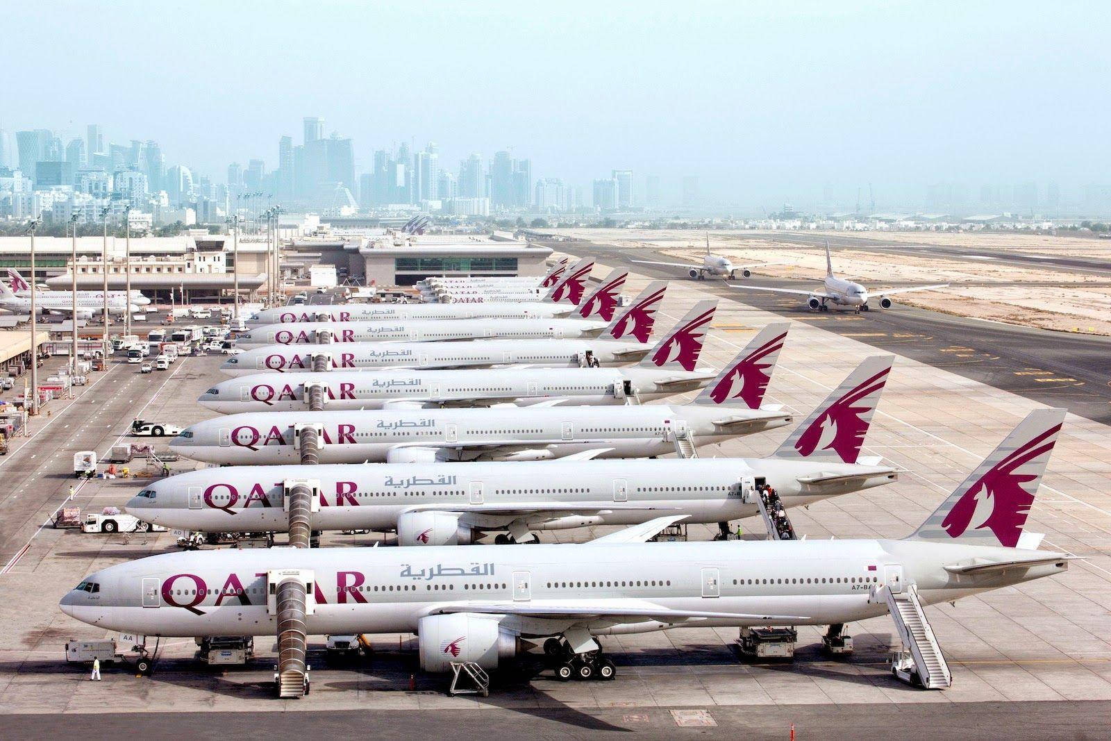 Qatar 桌布 壁紙 — 一排卡塔爾航空飛機停泊在機場閘口，背景是現代化的城市天際線。
