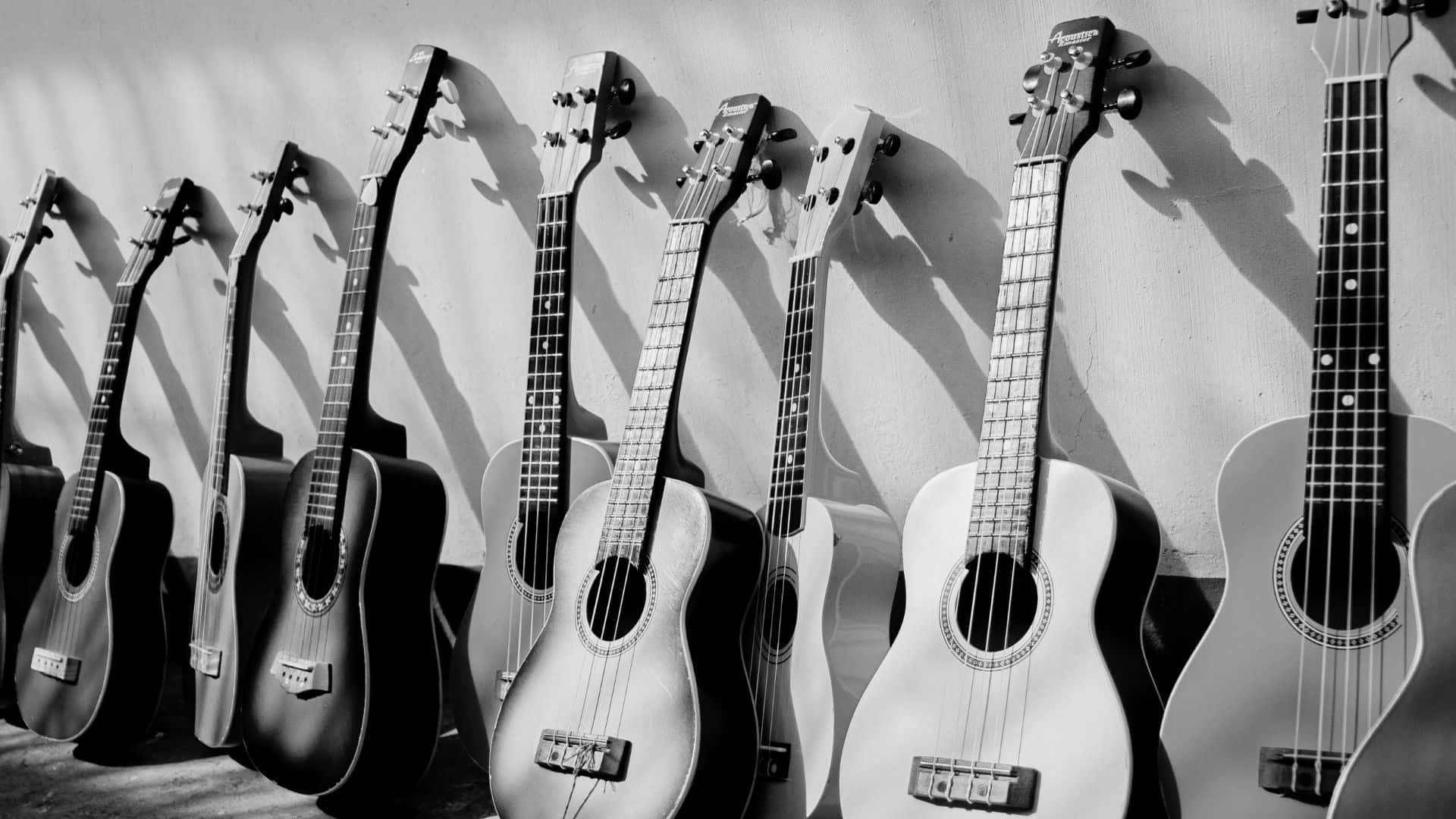 Black And White Guitar 桌布 壁紙 — 一排原聲吉他靠牆而立，投射出長長的陰影，呈現高對比度的黑白效果。