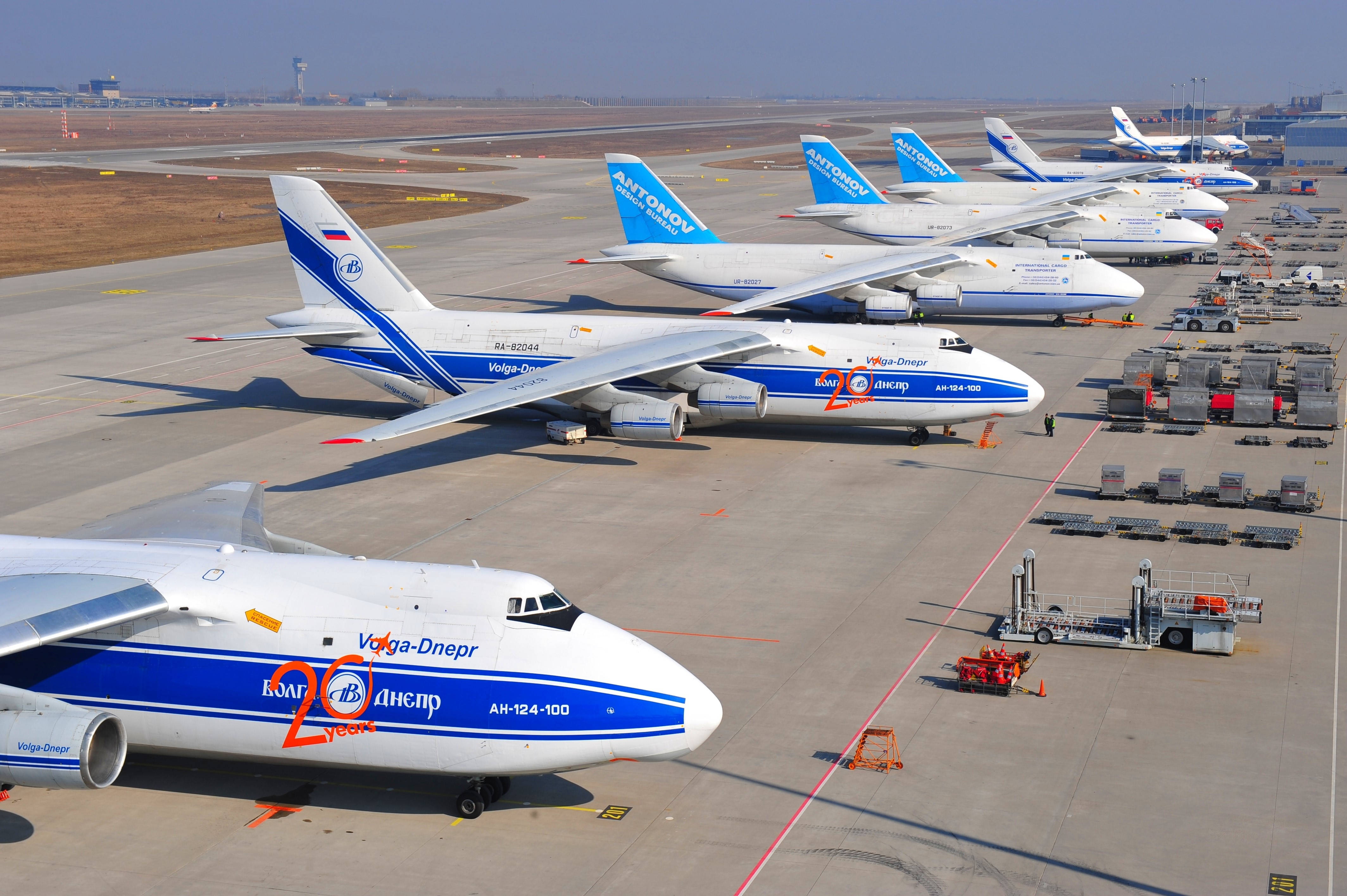 Airport 桌布 壁紙 — 一排大型白色和藍色安東諾夫貨機停放在陽光明媚的機場停機坪上，附近有地面設備。