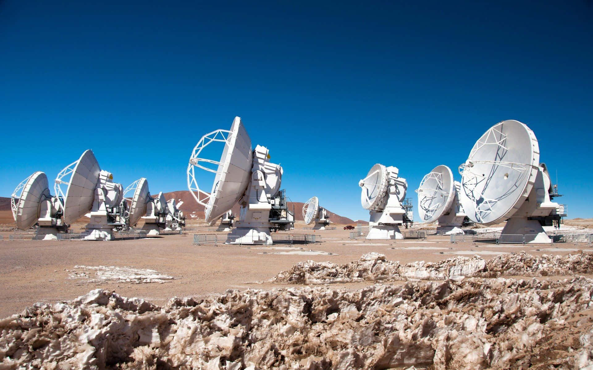 Radio Telescope 桌布 壁紙 — 一排大型白色無線電望遠鏡矗立在晴朗藍天下的貧瘠沙漠中。
