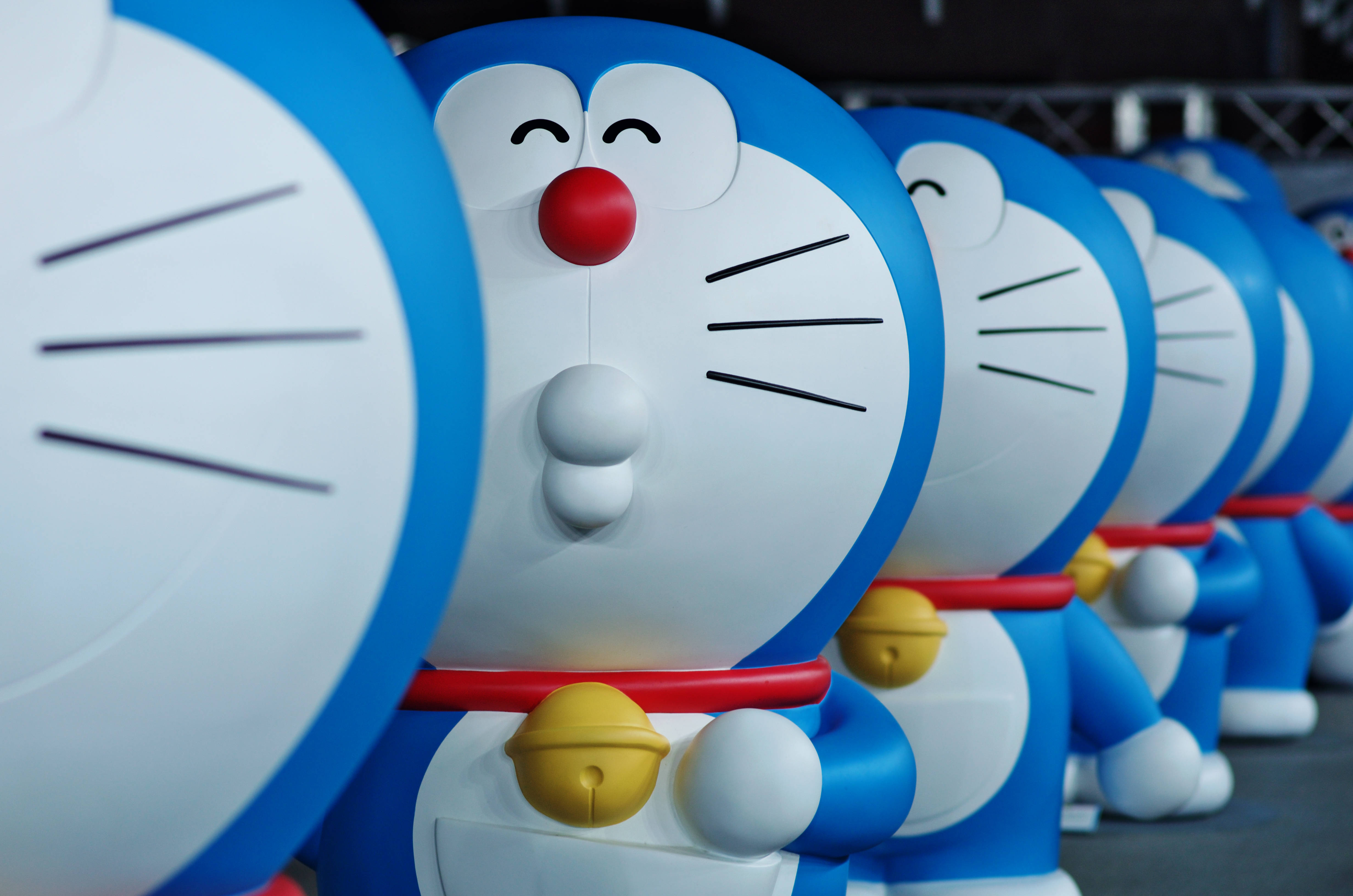 Doraemon 桌布 壁紙 — 一排大型藍白色哆啦A夢雕像，紅色鼻子和黃色鈴鐺，處於淺景深中。