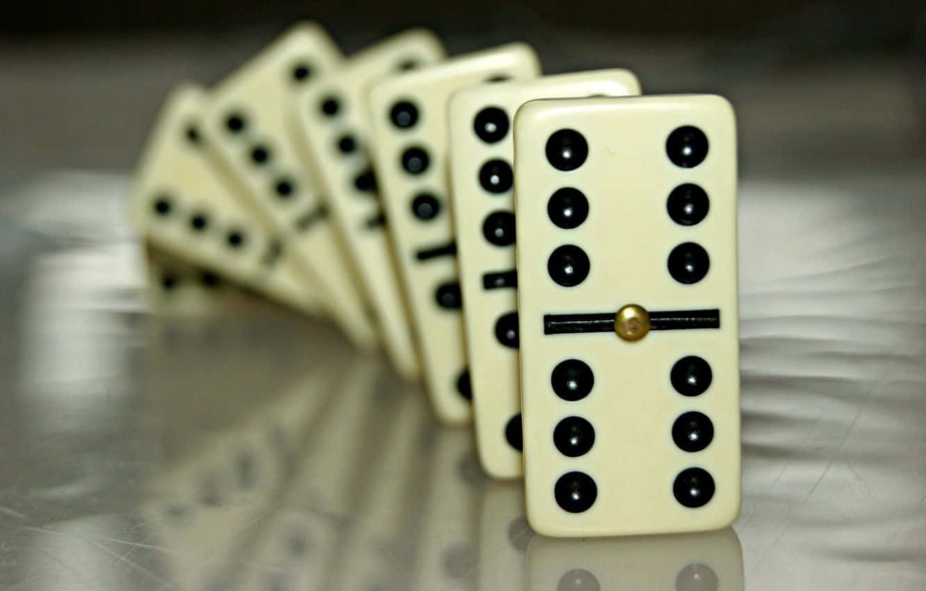 Domino 桌布 壁紙 — 一排奶油色多米諾骨牌，帶有黑色圓點和金色中心部件，放置在反光的金屬表面上。