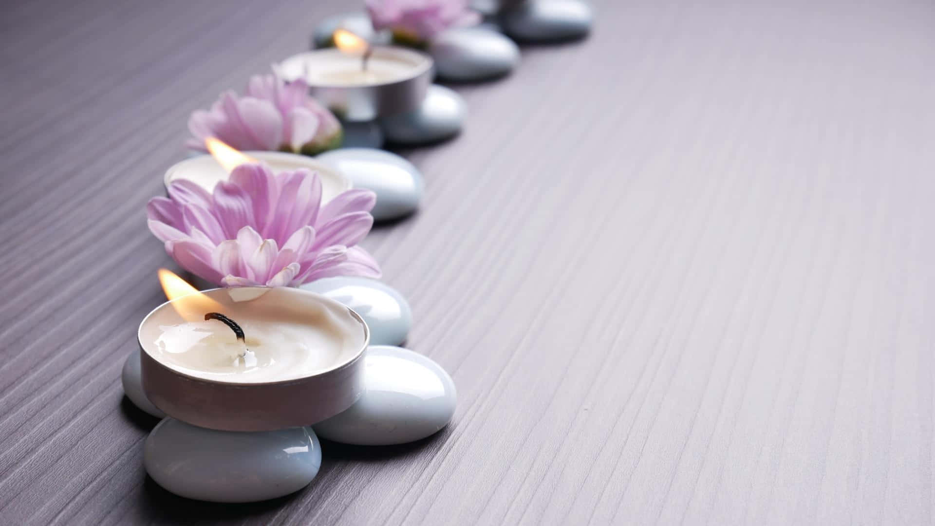 禪 桌布 壁紙 — 一排寧靜的對角線上的點燃茶燭和粉紅花朵，安放在木質表面上的光滑灰色石頭上。