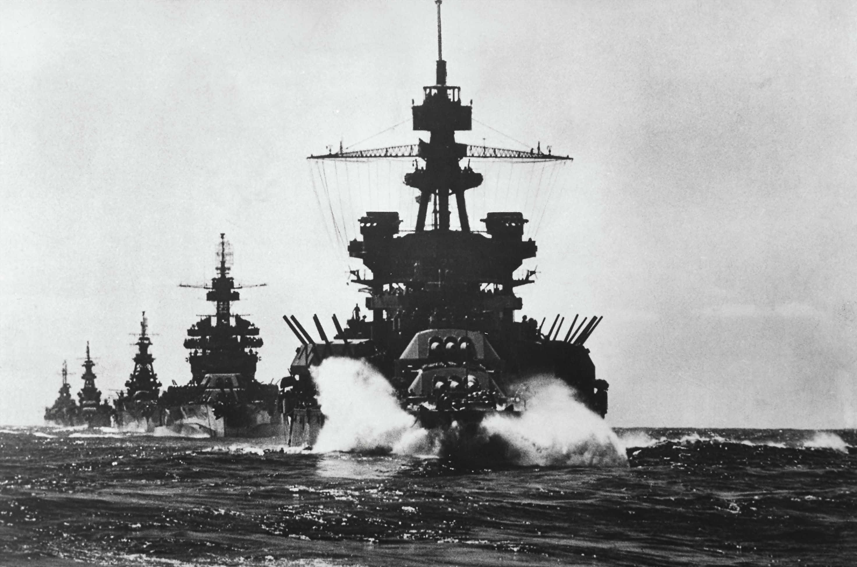 Battleship 桌布 壁紙 — 一排巨型戰艦劃過波濤洶湧的海面，在陰天留下白色航跡。