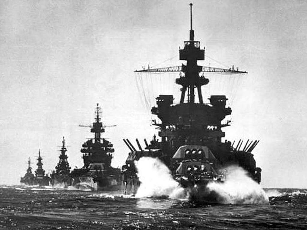 戰爭動圖 桌布 壁紙 — 一排巨大的戰艦劃過波濤洶湧的海面，在船頭後留下白色尾跡，呈現出一張清晰的黑白照片。
