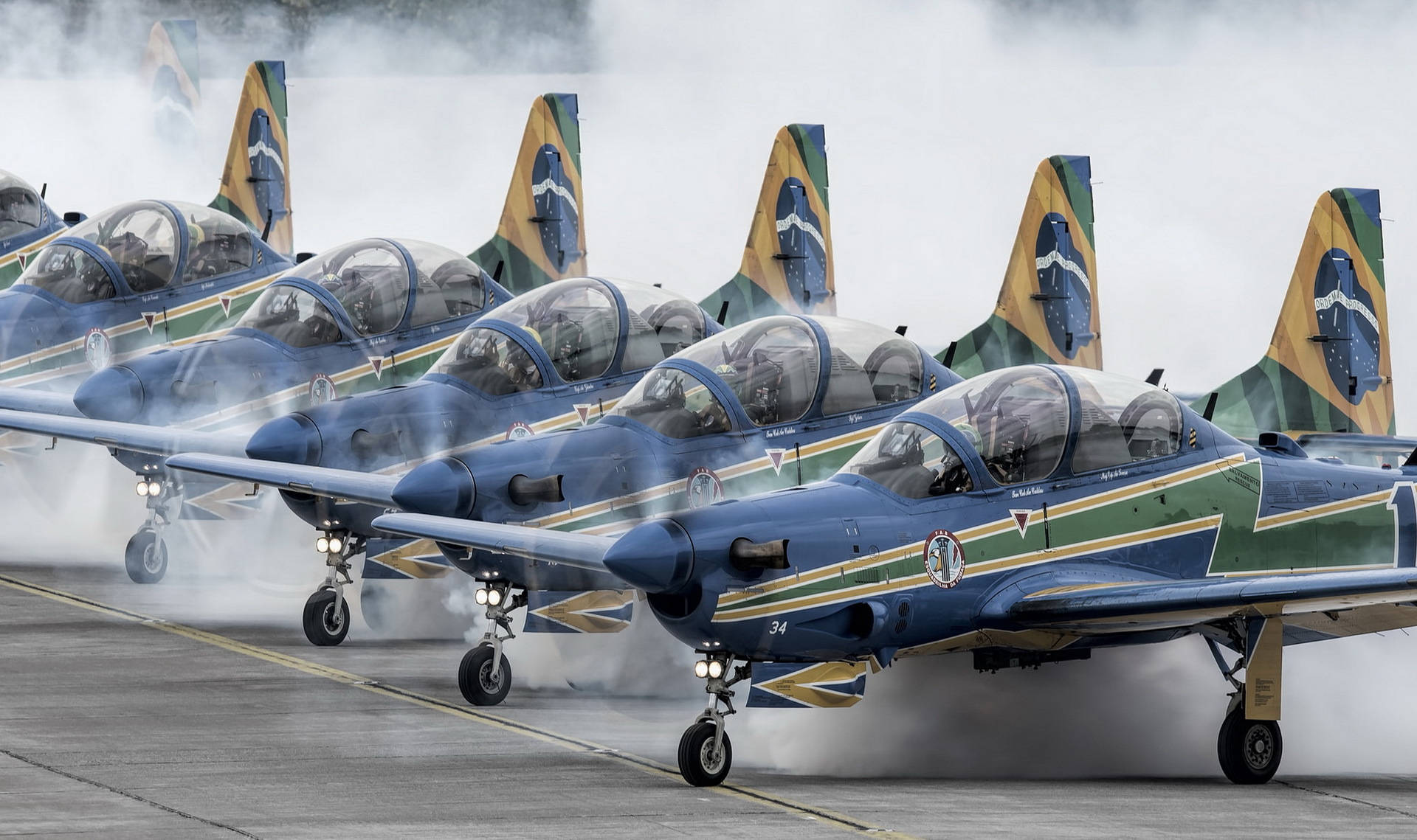 Air Force 桌布 壁紙 — 一排巴西軍用噴射機，機尾帶有國旗，在跑道上排列，引擎噴出煙霧。