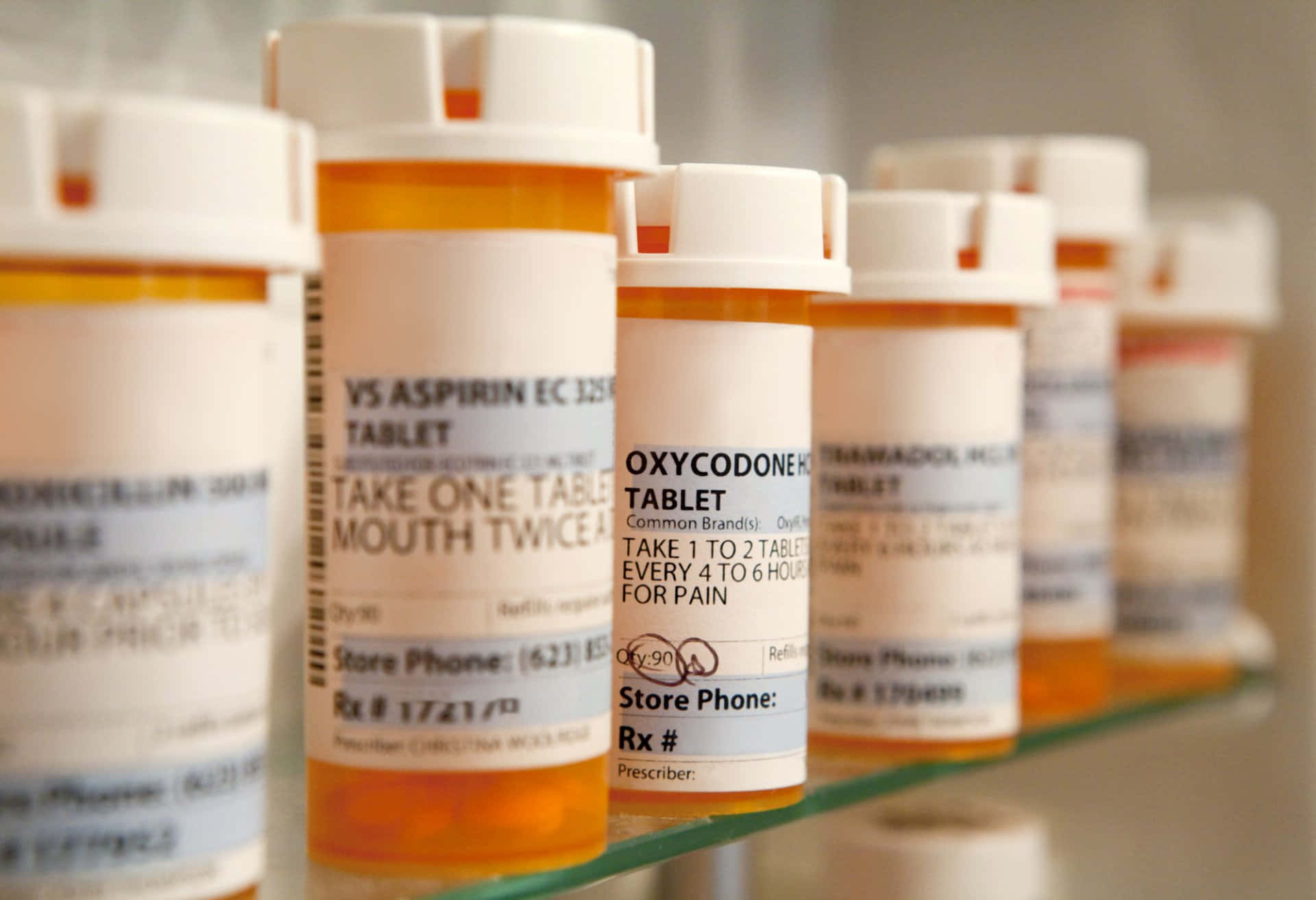 medicine 桌布 壁紙 — 一排帶有阿斯匹靈和奧施康定標籤的處方藥瓶放在藥房的玻璃架上。