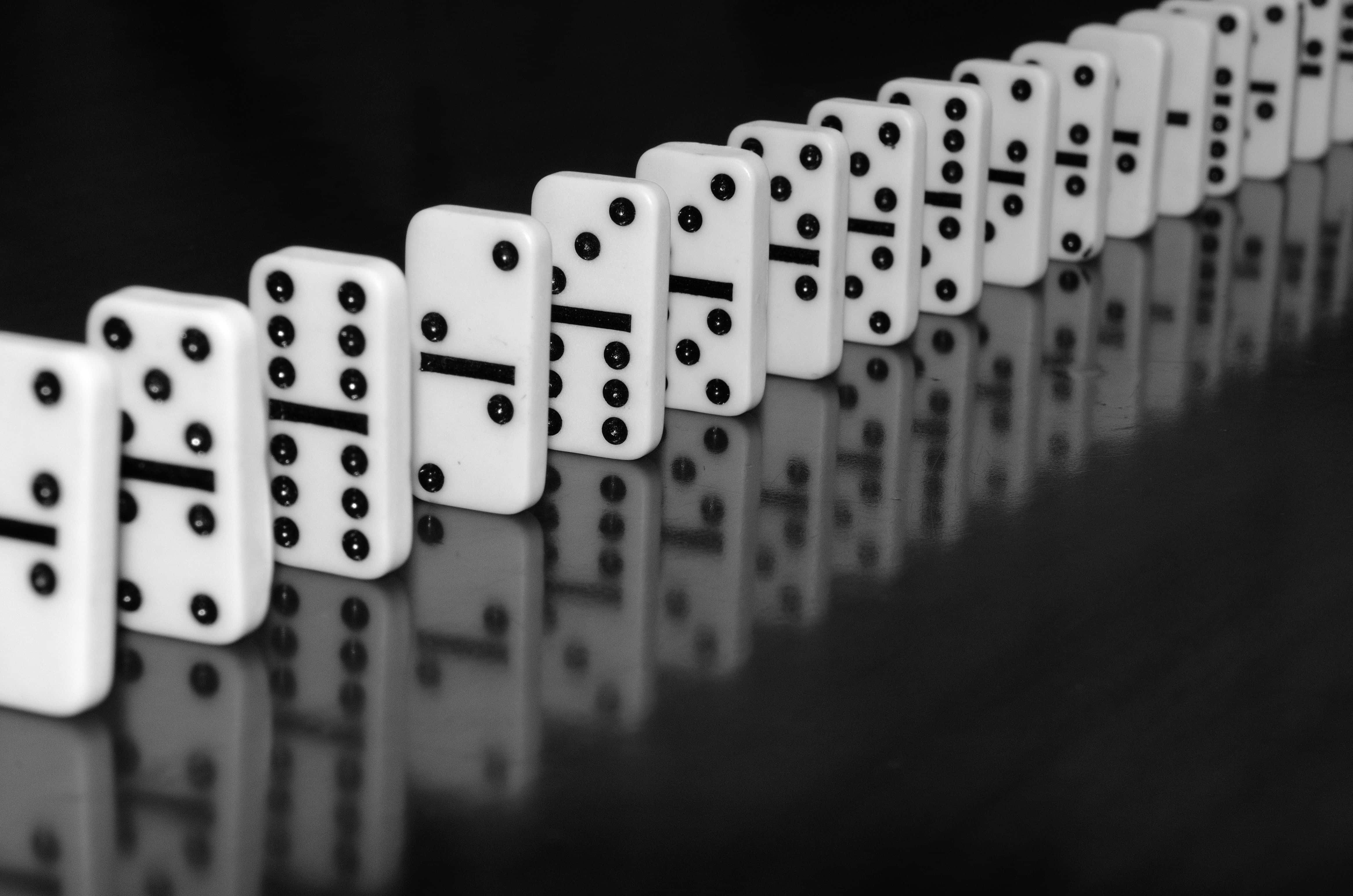 Domino 桌布 壁紙 — 一排帶有黑點的白色的多米諾骨牌在反光表面上以單色完美排列。