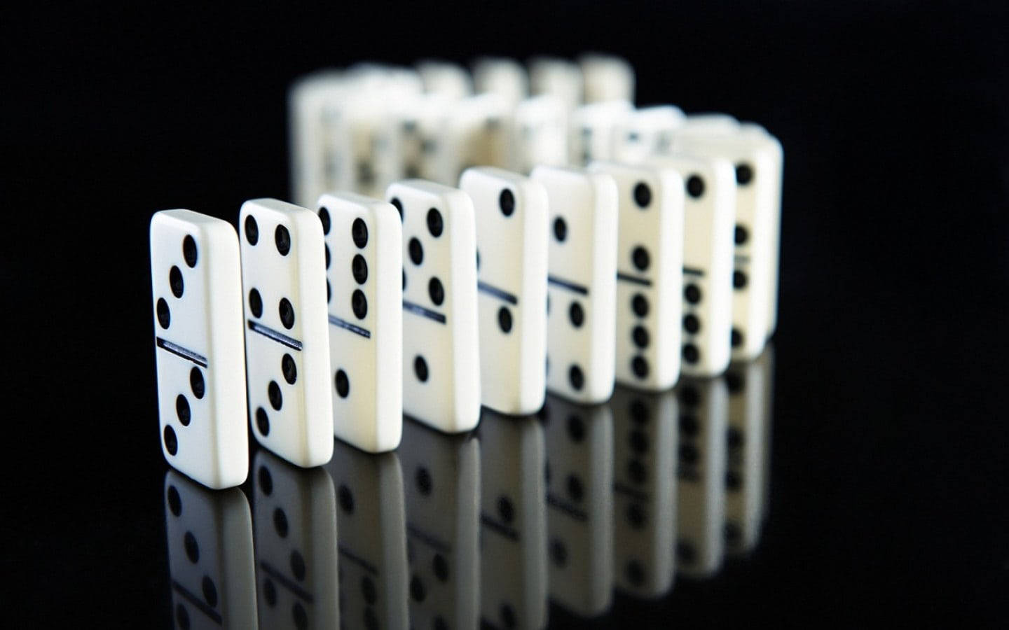 dominos 桌布 壁紙 — 一排帶有黑點的白色的多米諾骨牌豎立在反光的黑色表面上，準備倒下。