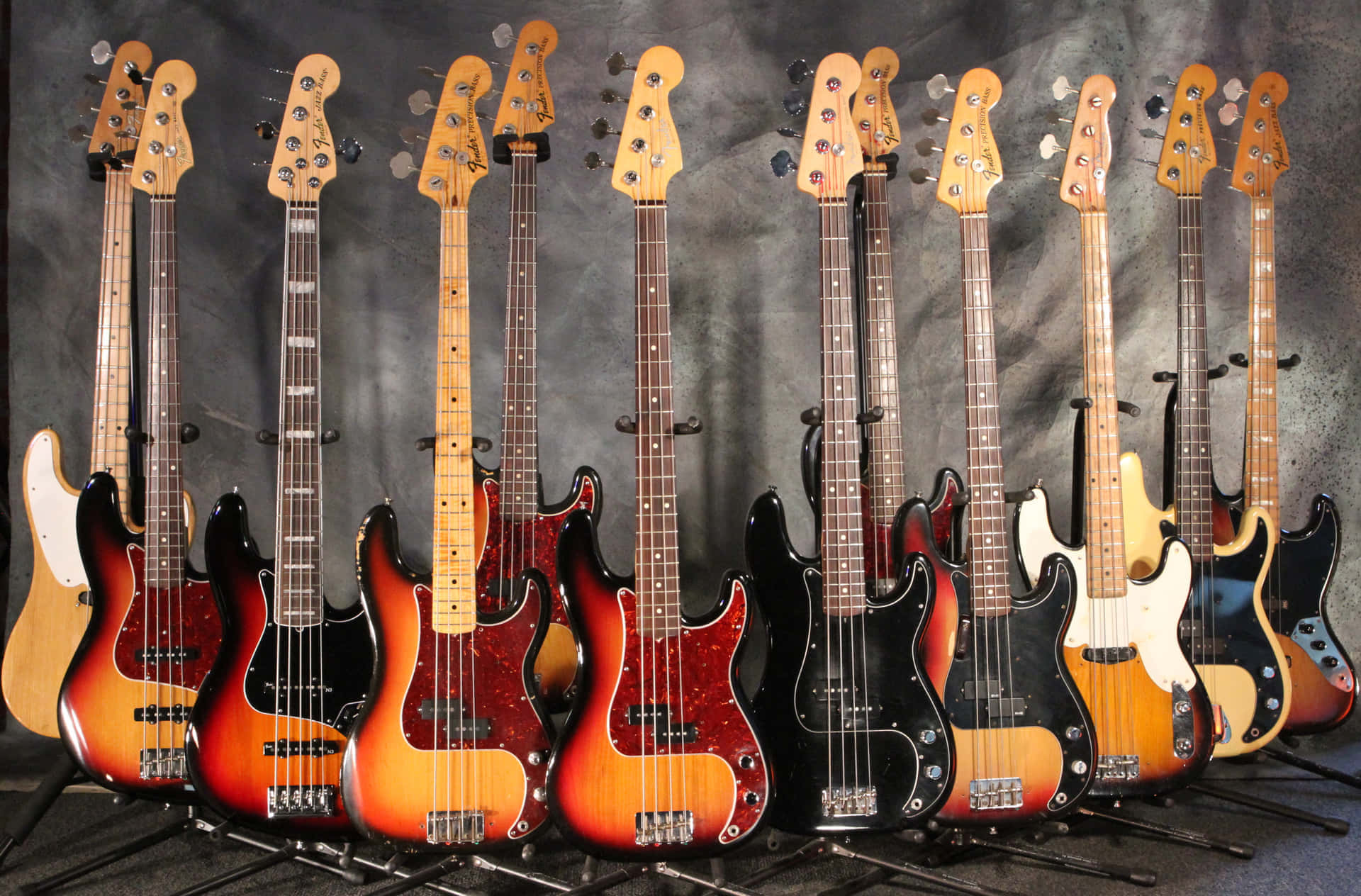 Guitar Aesthetic 桌布 壁紙 — 一排復古 Fender 貝斯吉他，採用漸變色和黑色飾面，自豪地矗立在紋理灰色背景前。