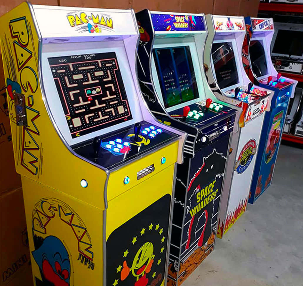 Arcade Games 桌布 壁紙 — 一排復古街機，包括小精靈和太空侵略者，在復古遊戲室中閃爍著彩色燈光。