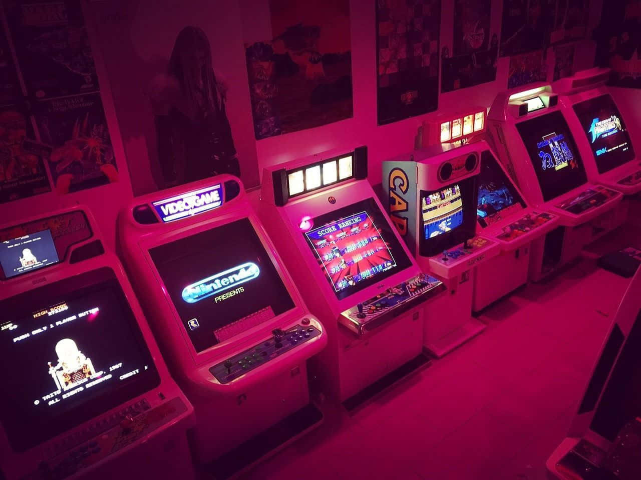 Arcade Aesthetic 桌布 壁紙 — 一排復古街機在強烈粉紅霓虹燈下發光，位於復古遊戲室內。