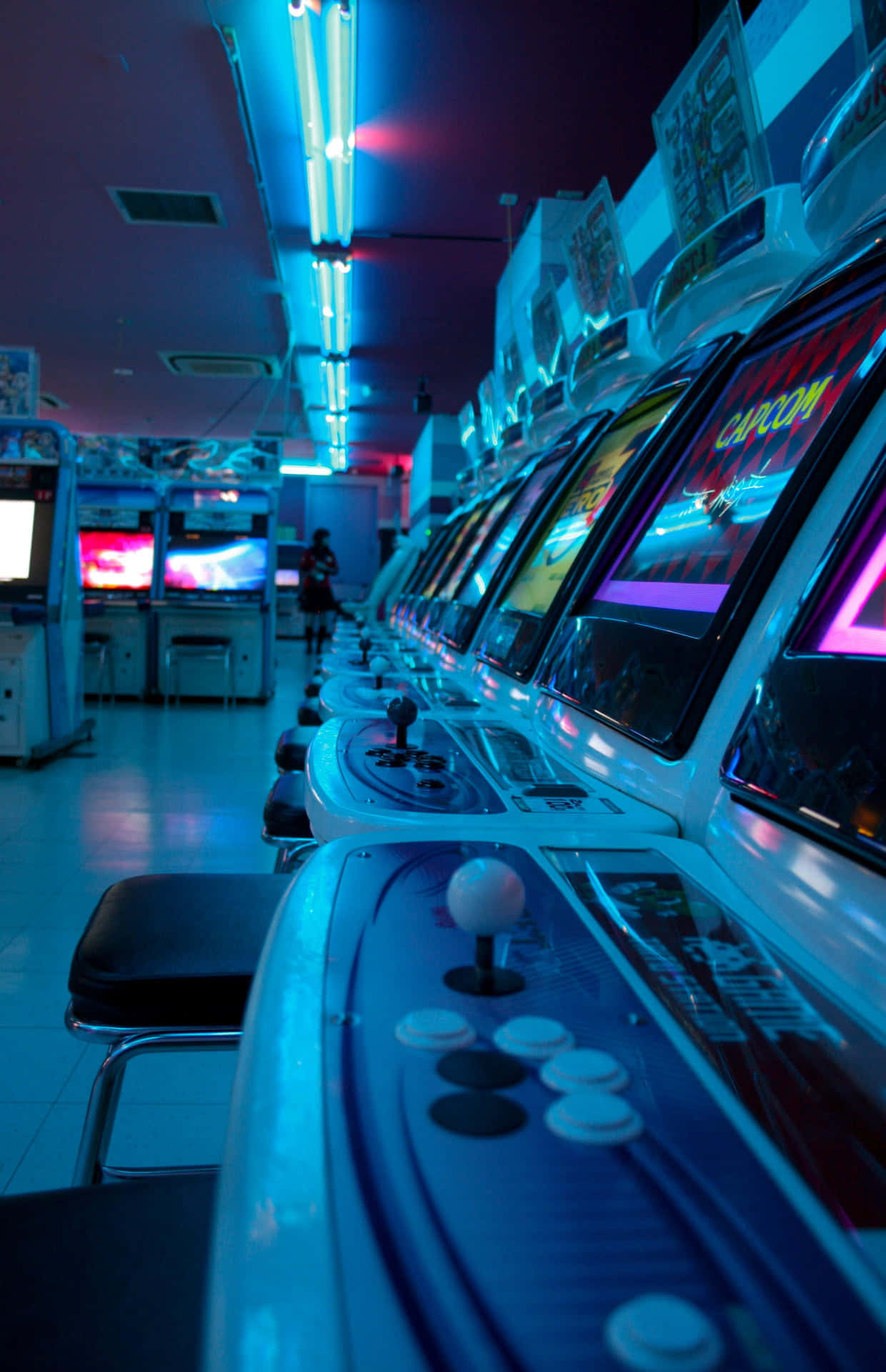 arcade 桌布 壁紙 — 一排復古街機在昏暗的復古遊戲廳中於霓虹燈下發光。
