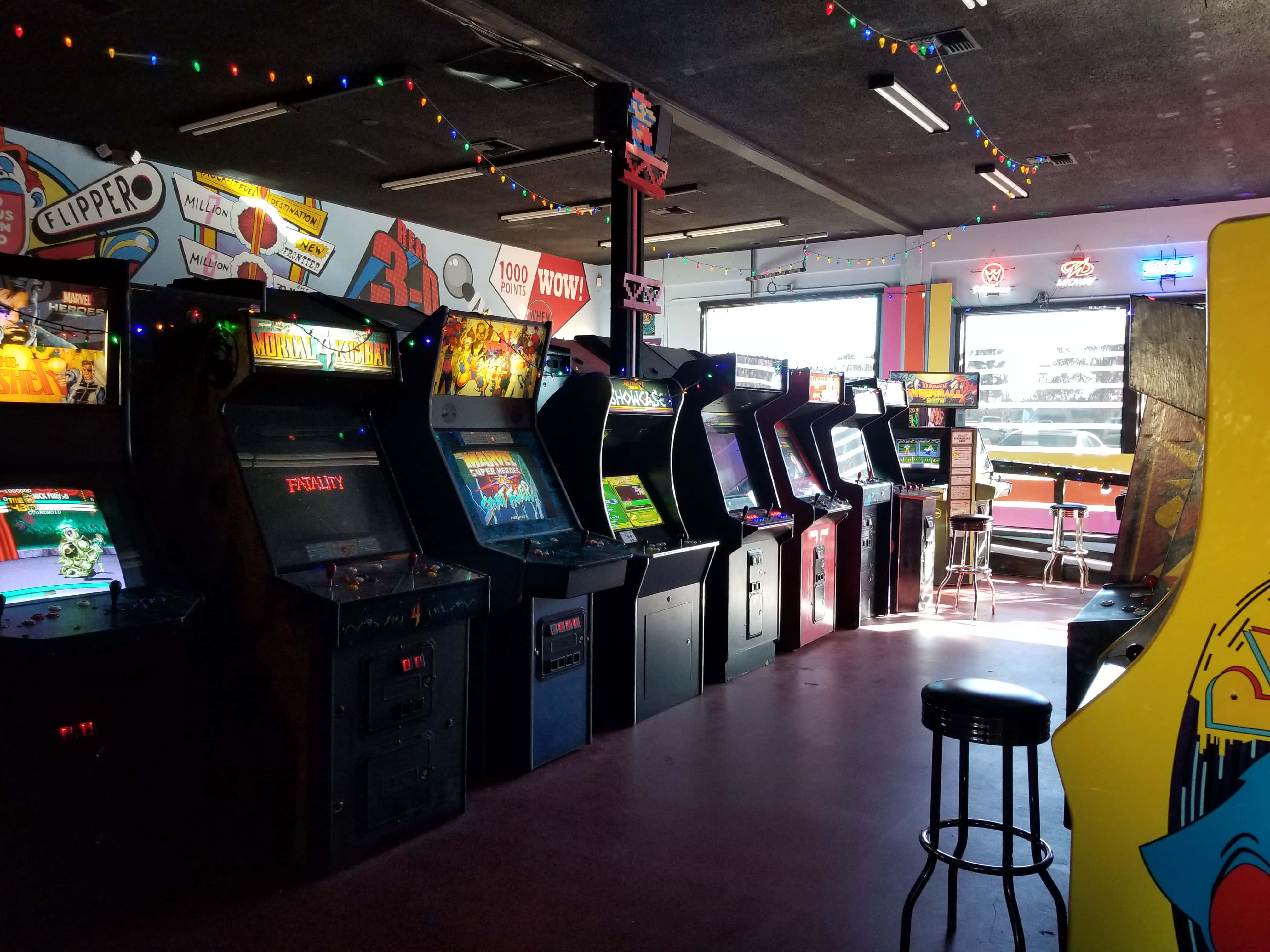 Arcade Games 桌布 壁紙 — 一排復古街機在色彩繽紛的燈串下閃耀，位於復古遊戲廳內。