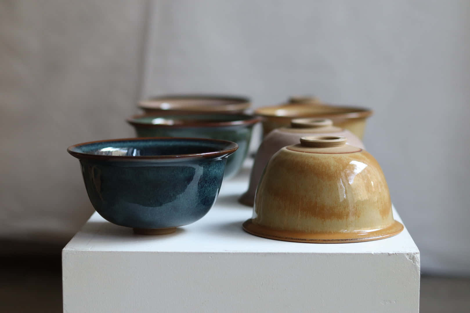 Ceramic 桌布 壁紙 — 一排手工製作的陶瓷碗，採用大地色調，放置在白色底座上，背景為柔和的灰色。
